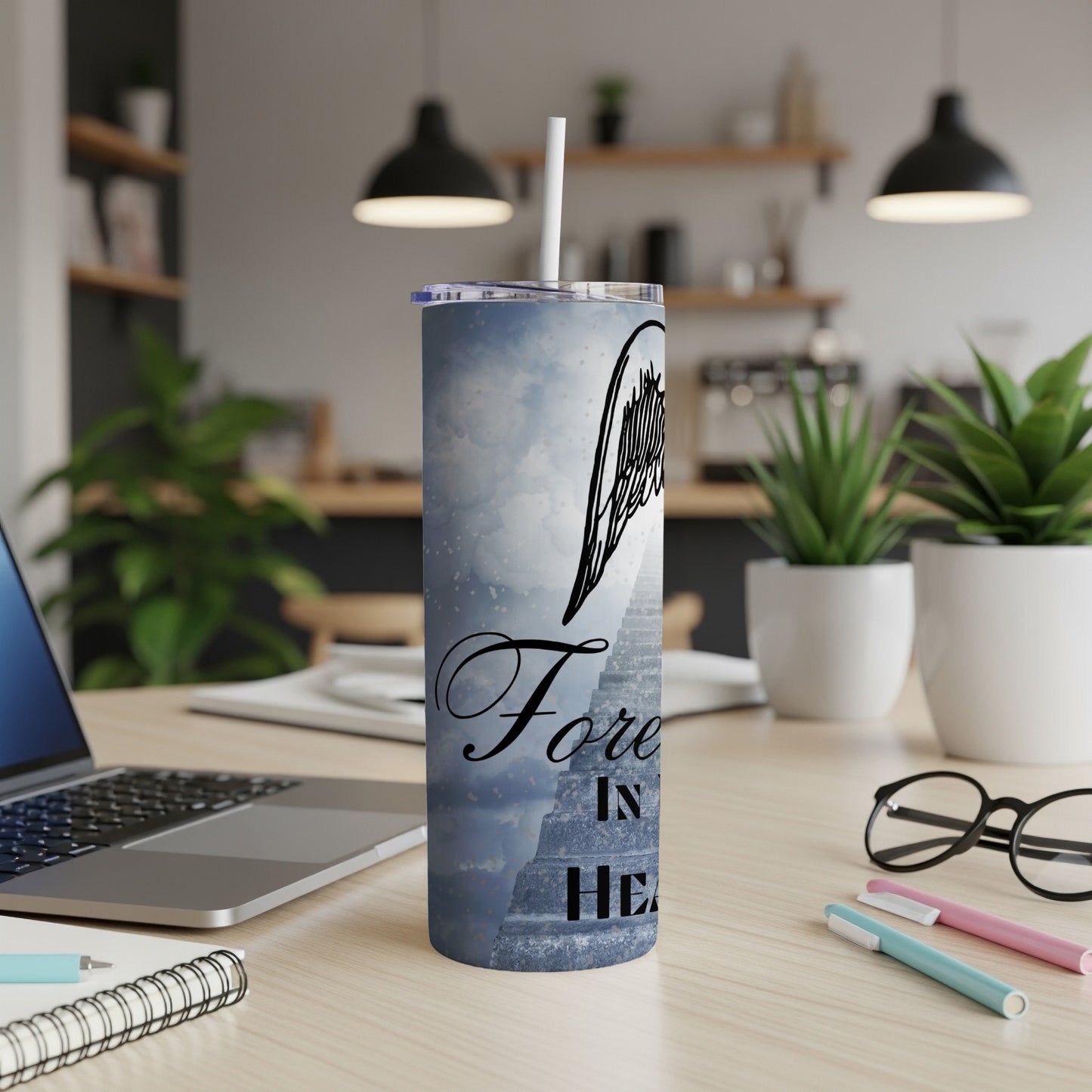 Tumbler with angel wings and text "Forever in Heaven" against a cloudy sky.