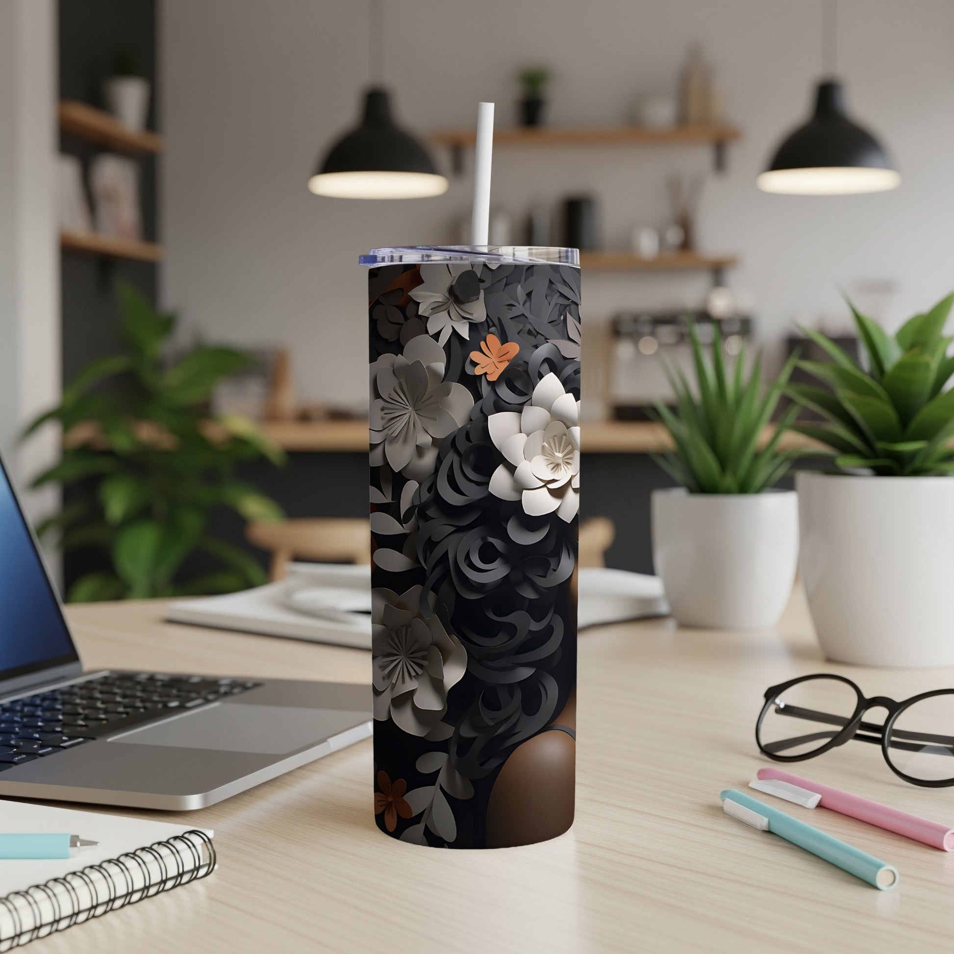 Black tumbler with floral pattern and white straw on a wooden desk.