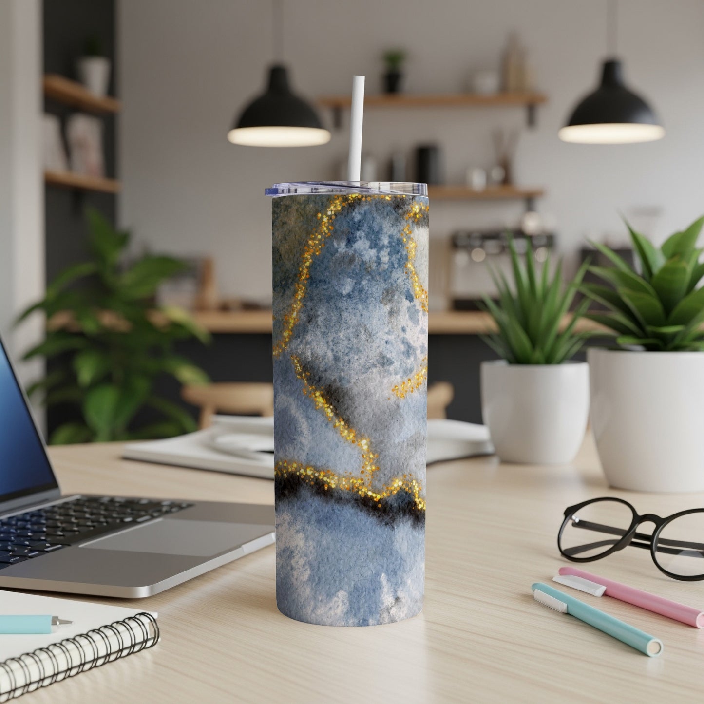 Blue and gold marbled tumbler with straw on a desk.