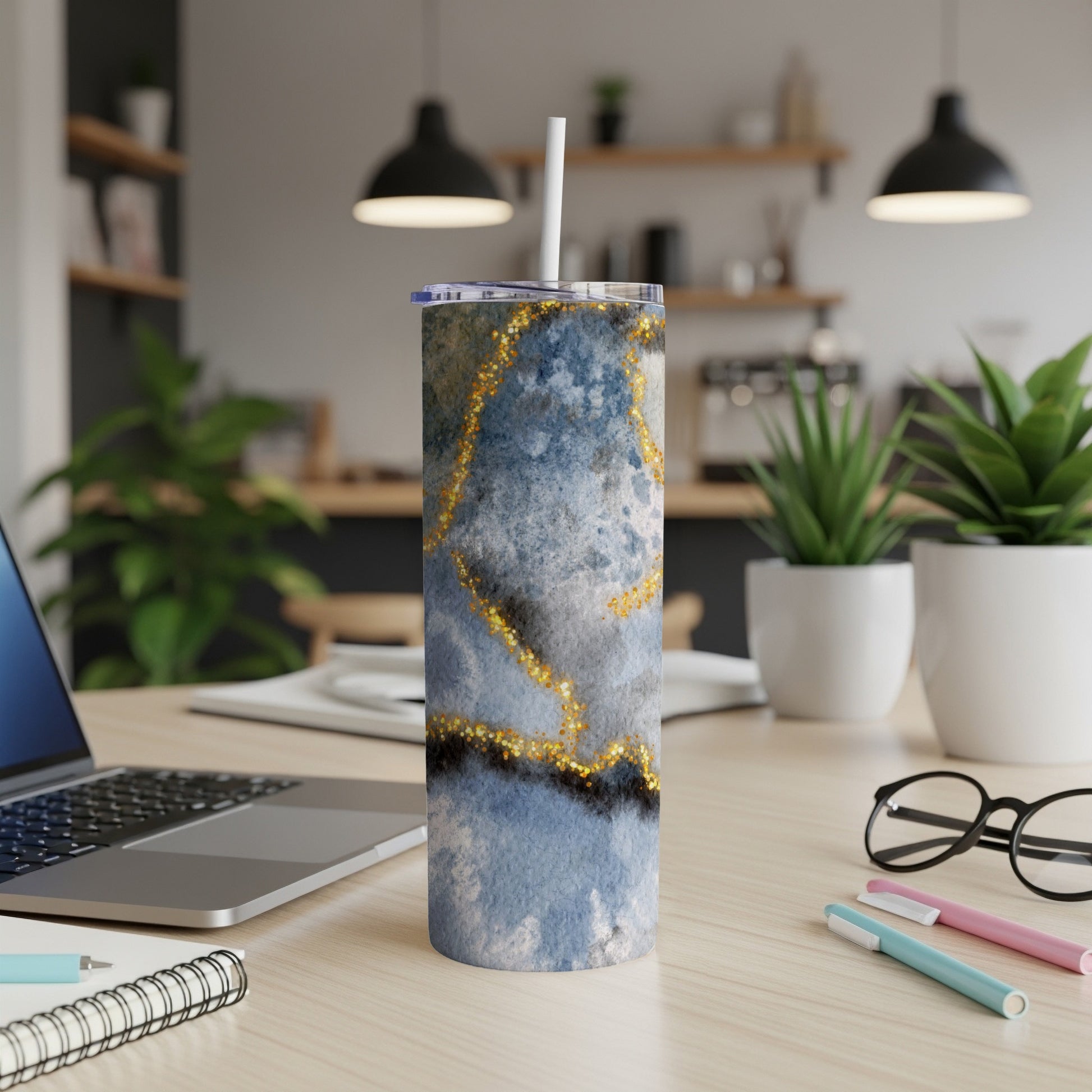 Blue and gold marbled tumbler with straw on a desk.