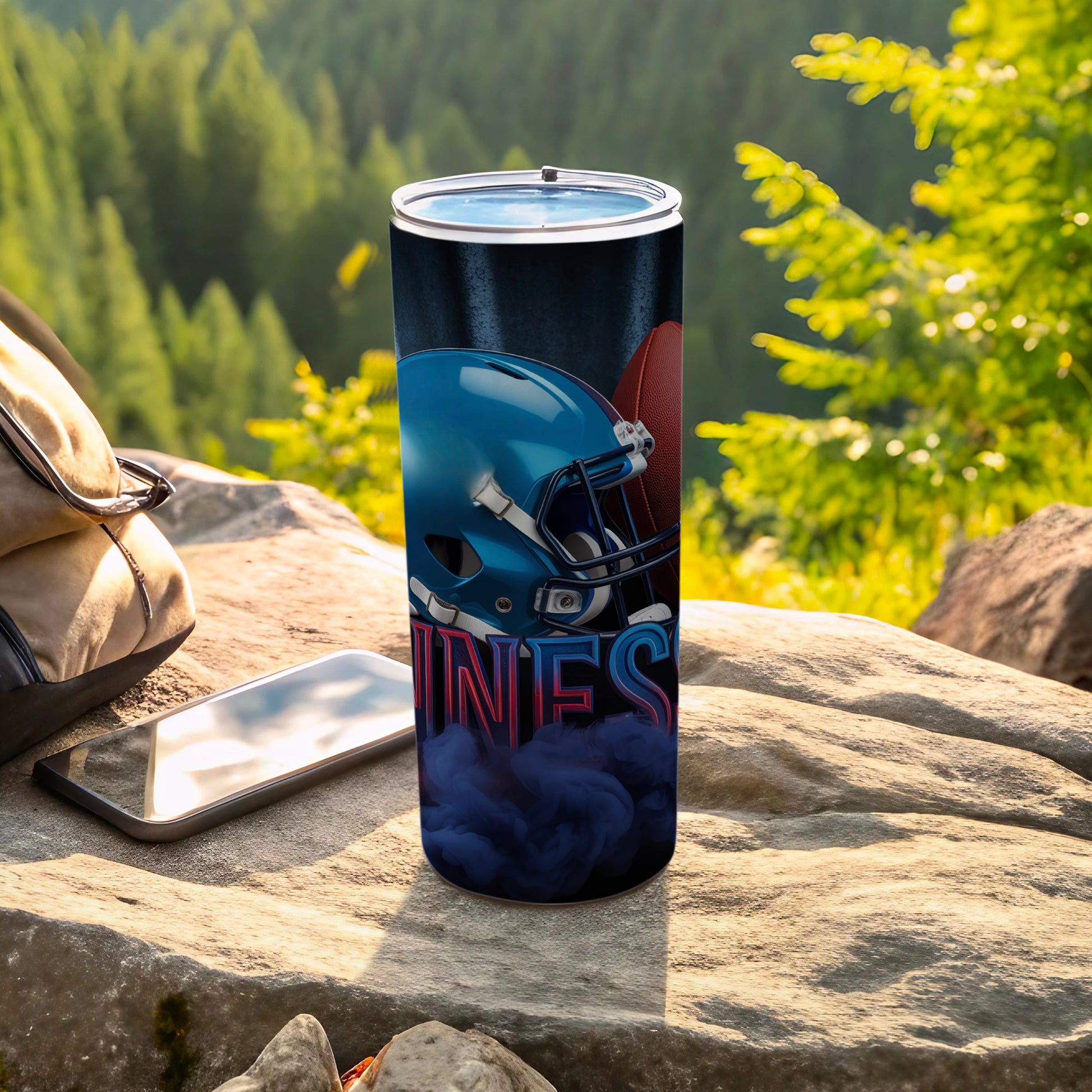 Tumbler with football helmet and "UNS" text on rocky surface near backpack and phone.