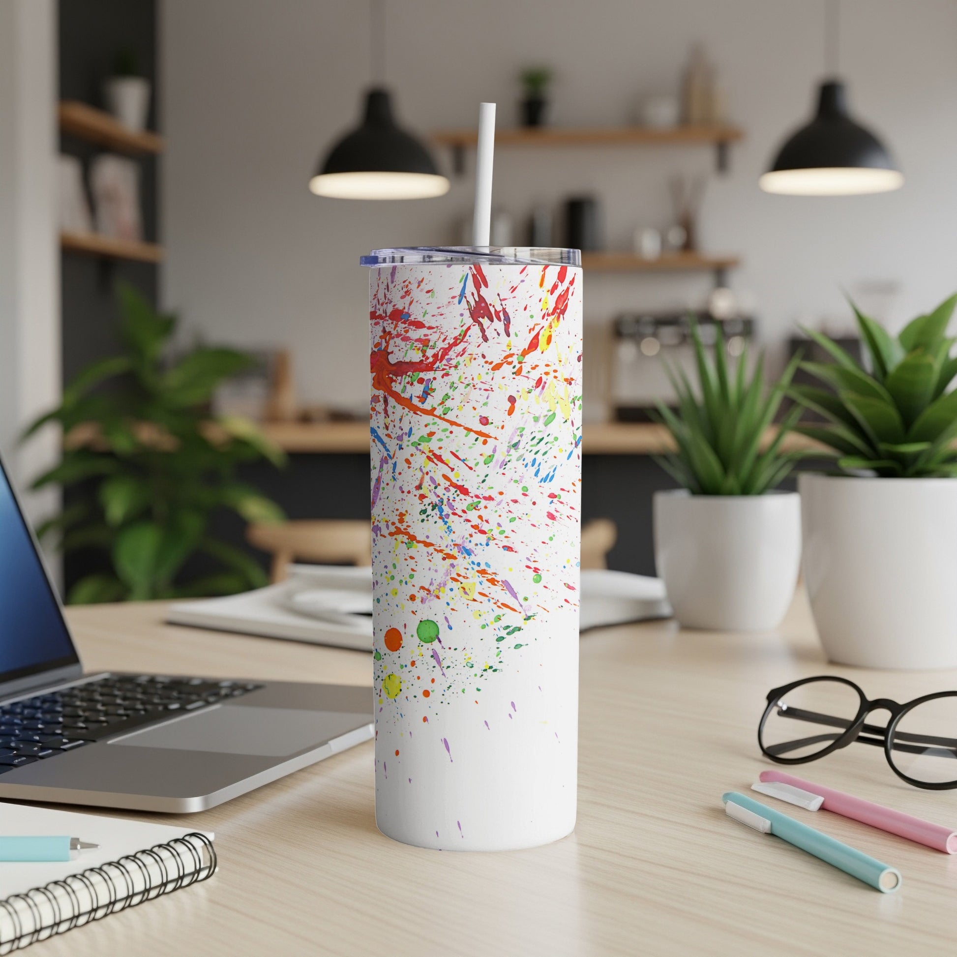 White tumbler with colorful paint splatters, straw, and desk accessories.