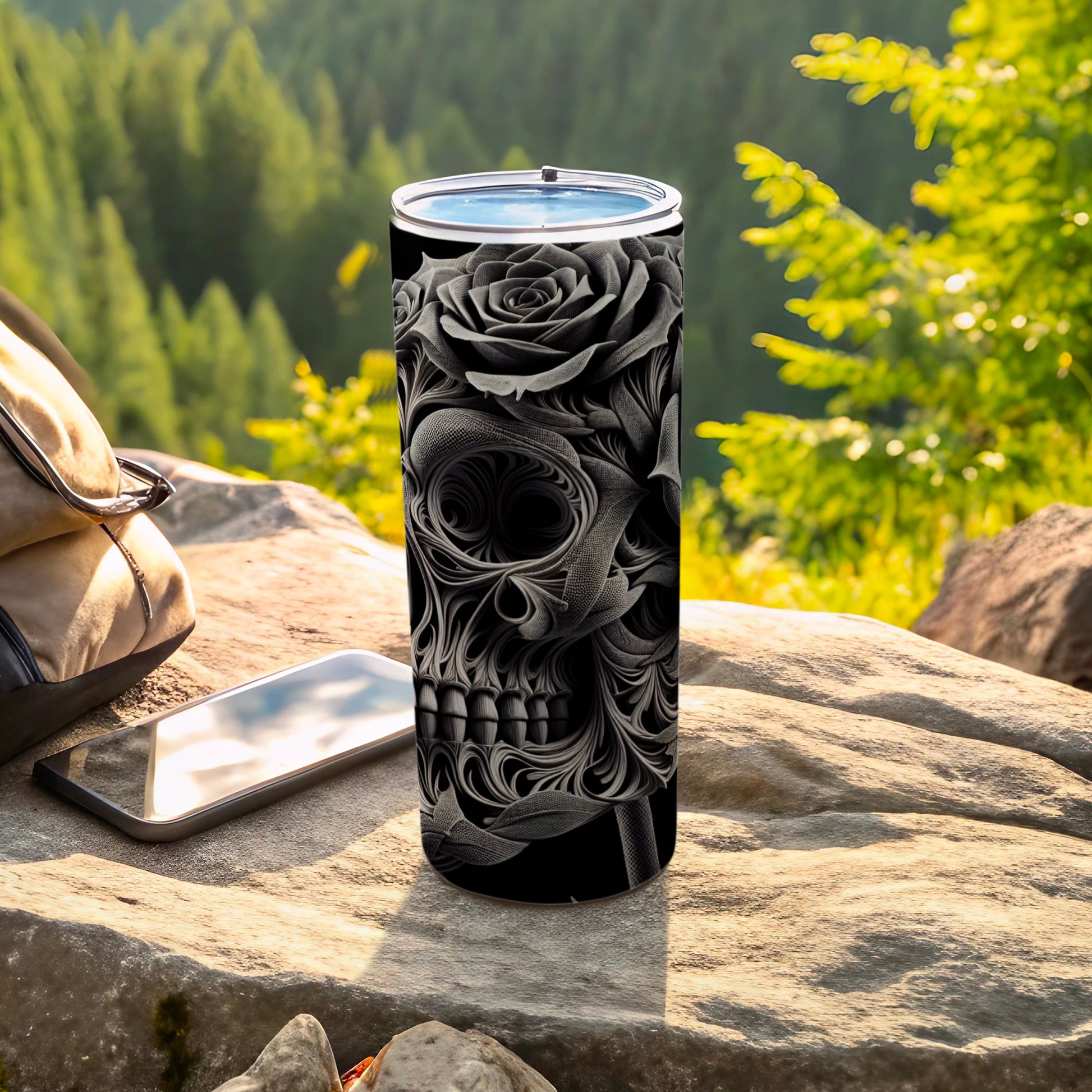 Black tumbler with a skull and rose design, resting on a rock.