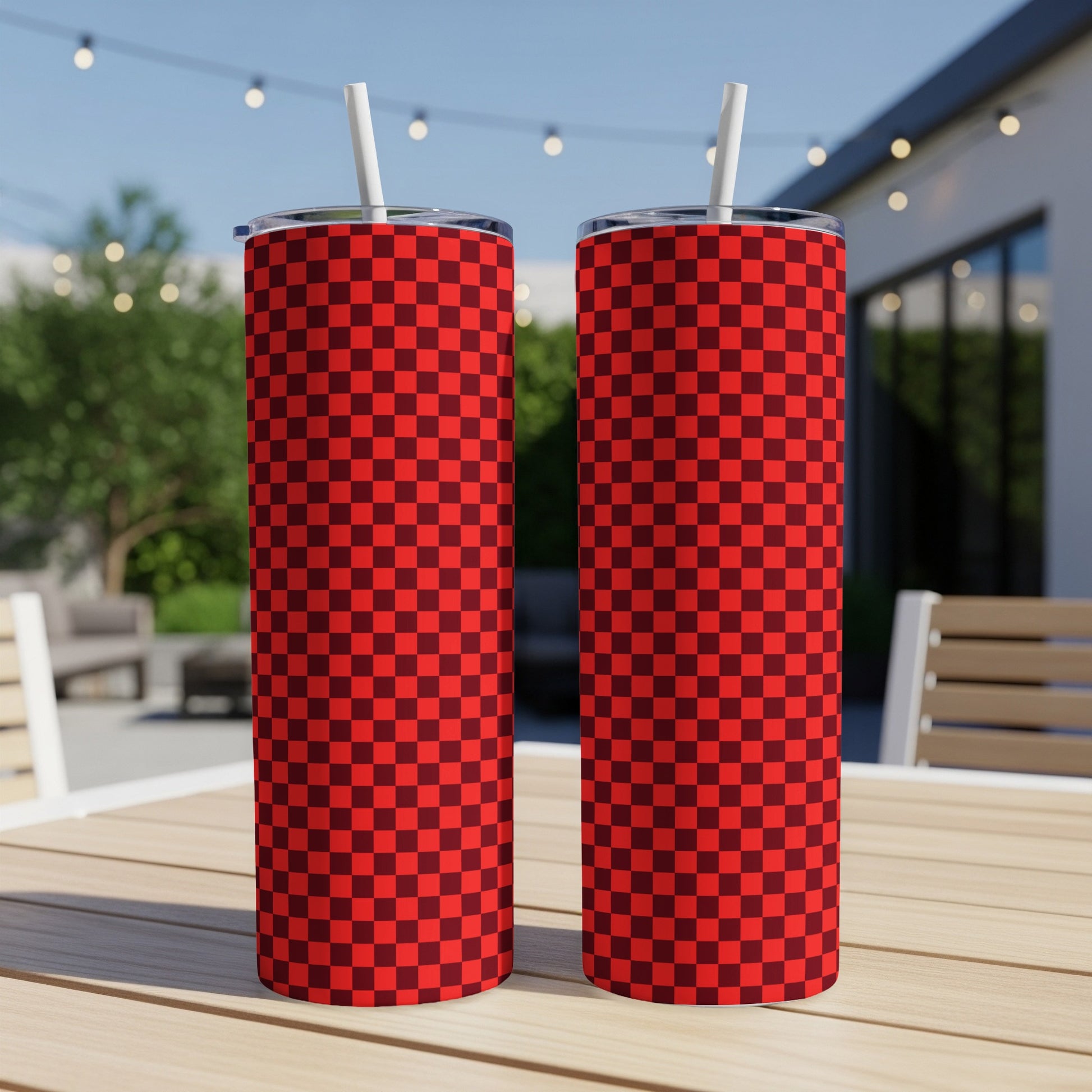 Two red and dark red checkered tumblers with straws on a table.