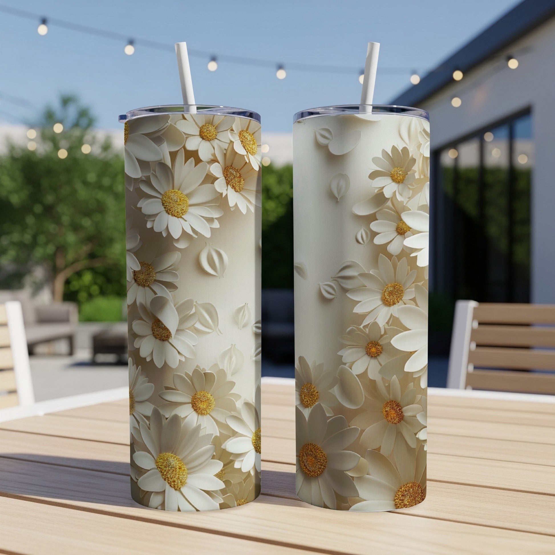 Two white floral tumblers with straws on a wooden table outdoors.