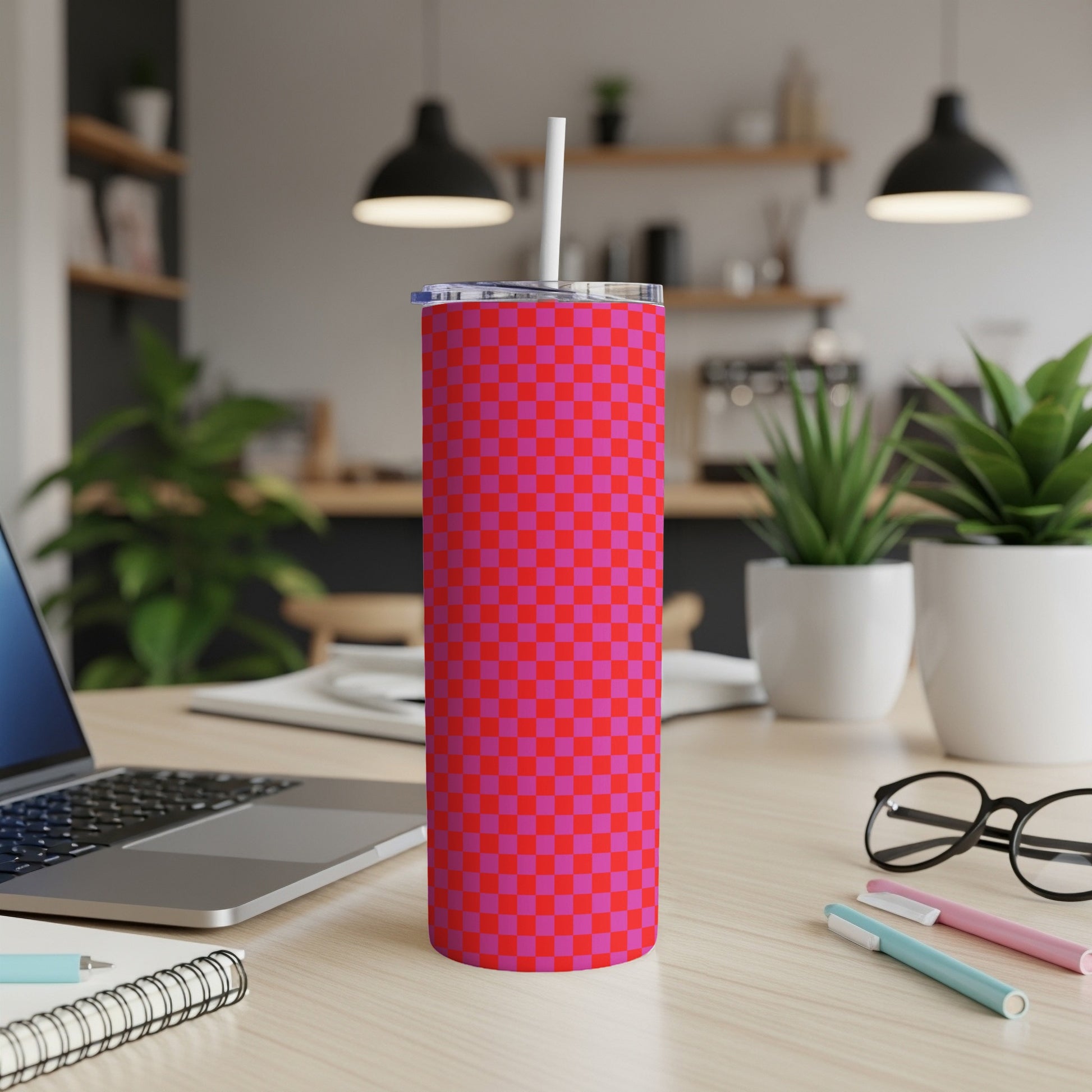 Checkerboard pattern tumbler with lid and straw on a desk.