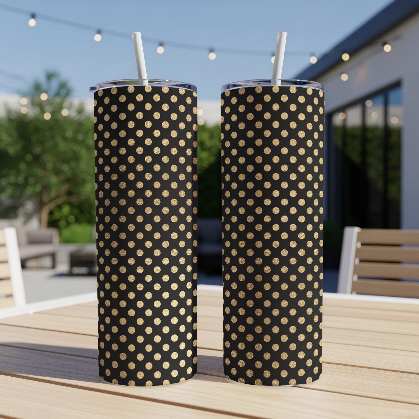 Two black tumblers with gold polka dots and white straws sit on a wooden table.