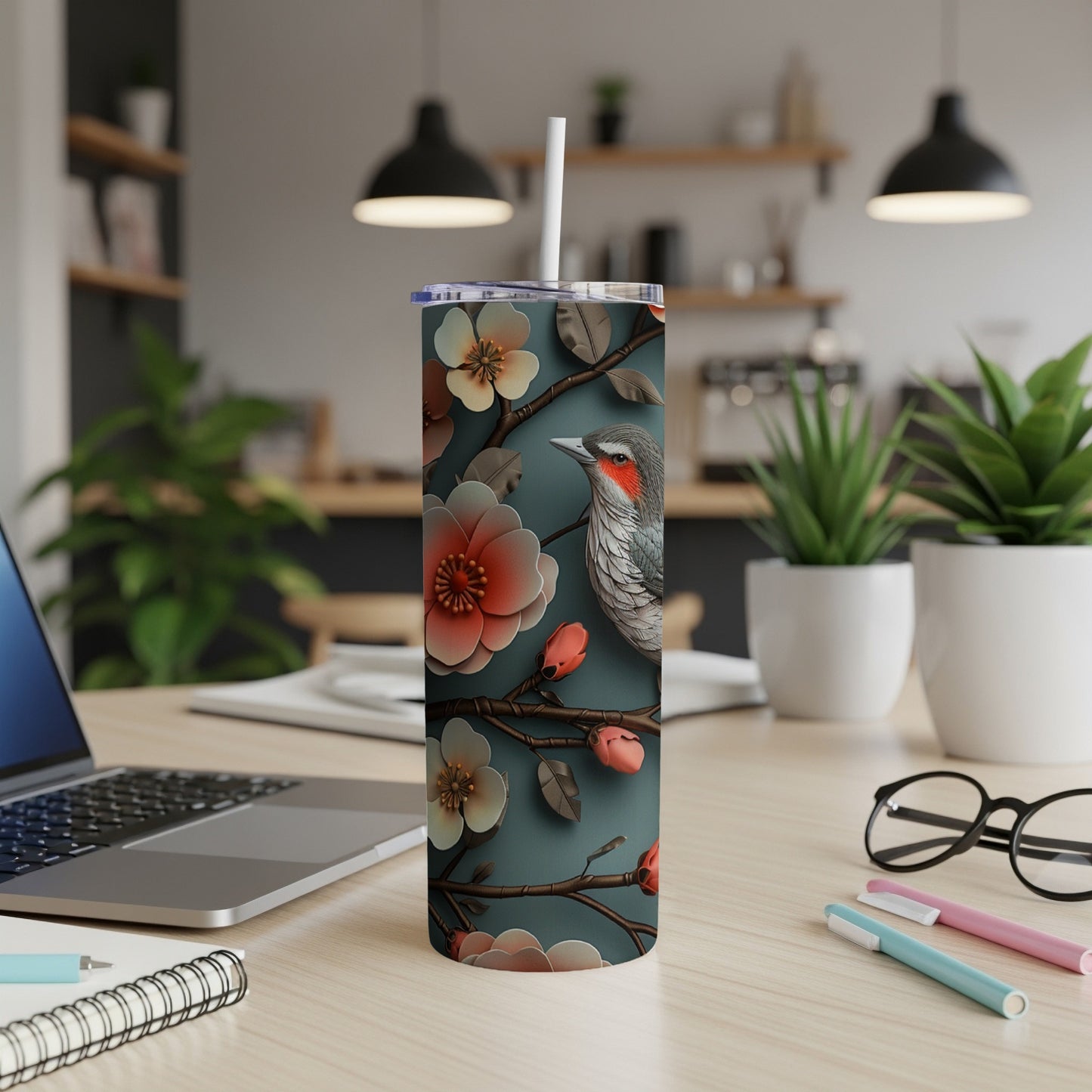 A tumbler with a bird and floral design on a desk.