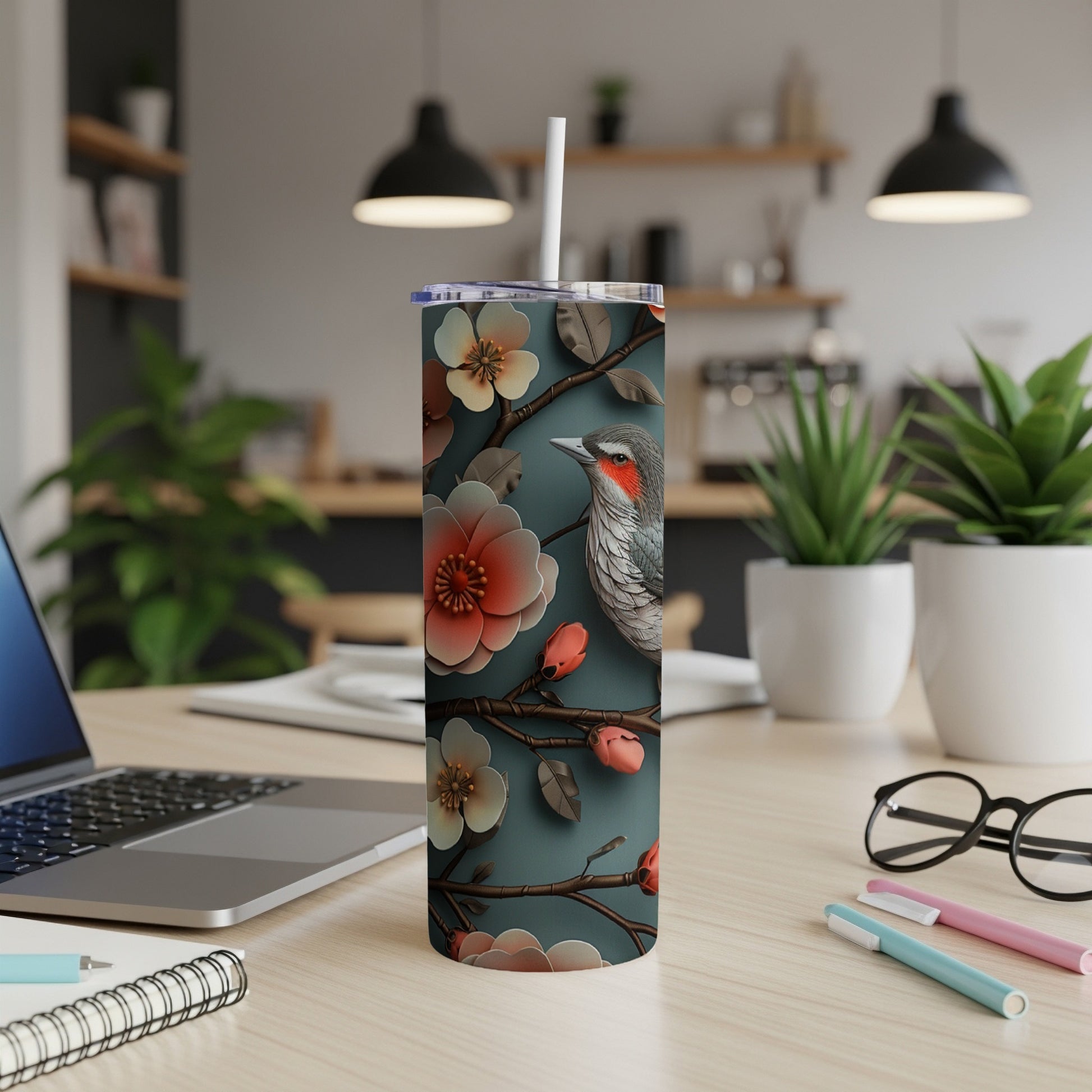 A tumbler with a bird and floral design on a desk.