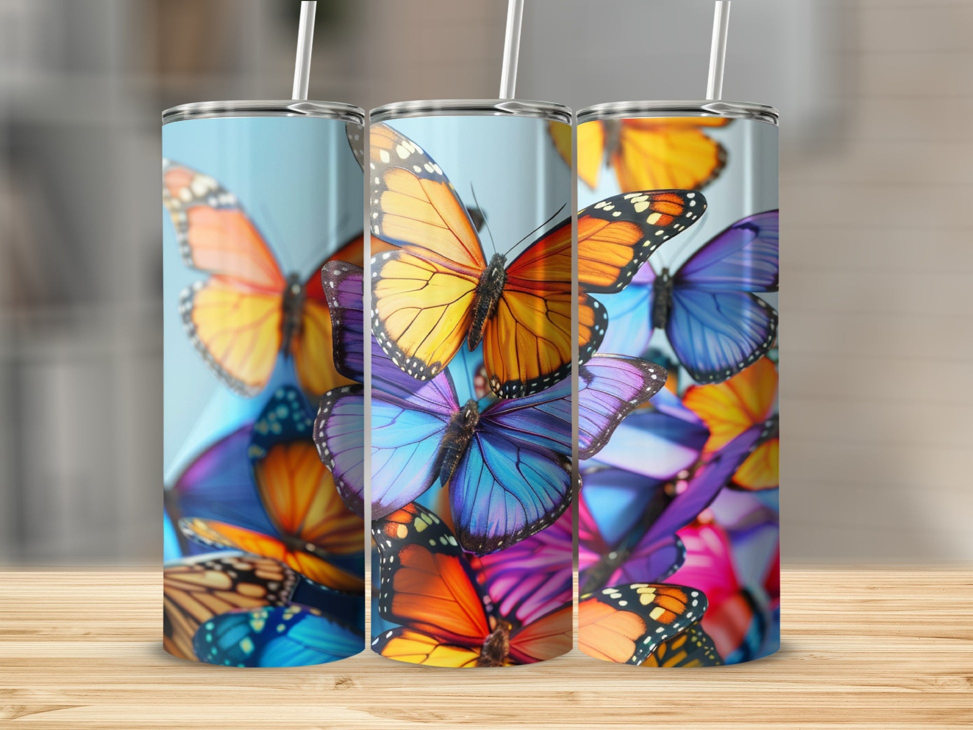 Three tumblers featuring colorful butterflies against a blurred background.
