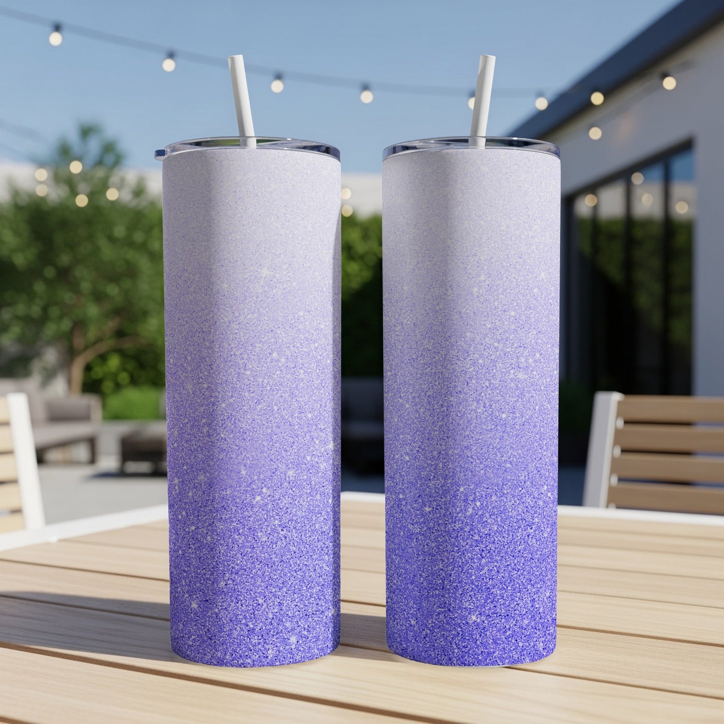 Two tall tumblers with purple to white glitter gradient and straws sit on a table.