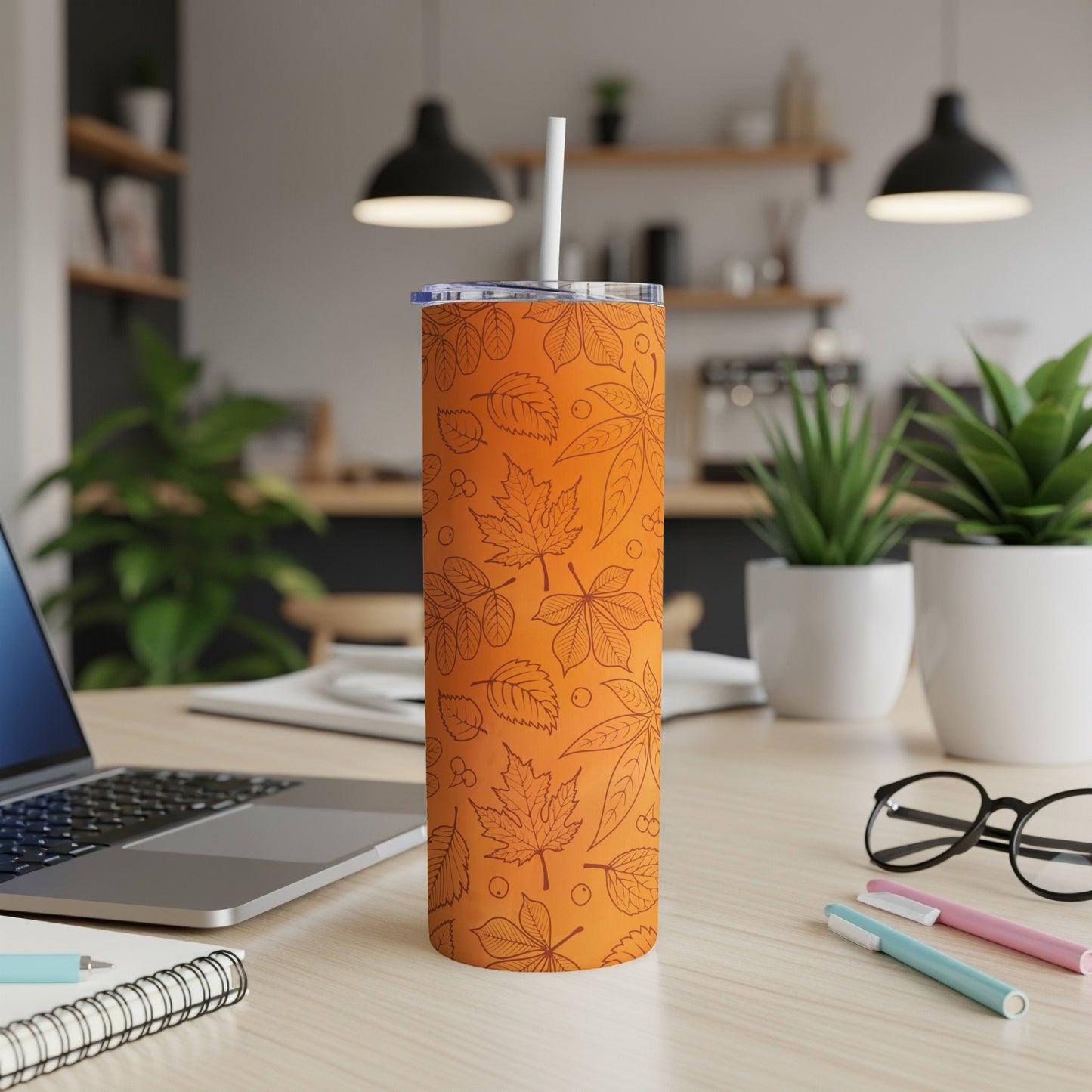 Orange tumbler with a falling leaves pattern, on a desk.