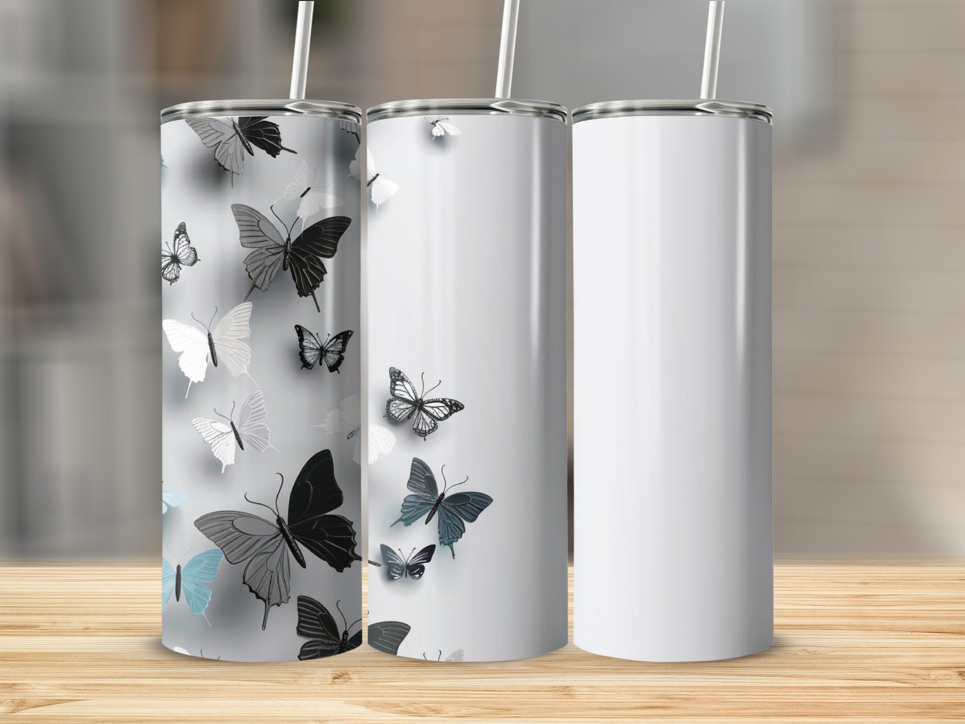 Three blank tumblers with a butterfly design on one, set on a wooden table.