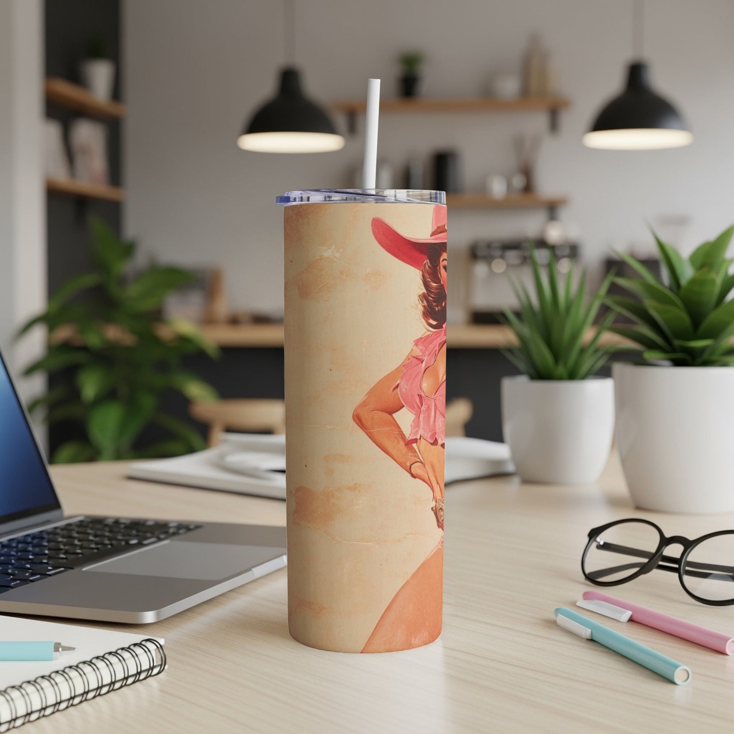 Cowgirl illustration on a tumbler with a straw, on a desk.