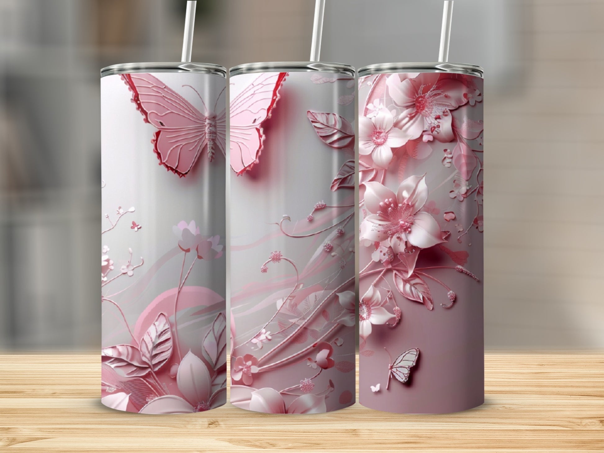 Three pink butterfly and floral patterned tumblers on a wooden surface.