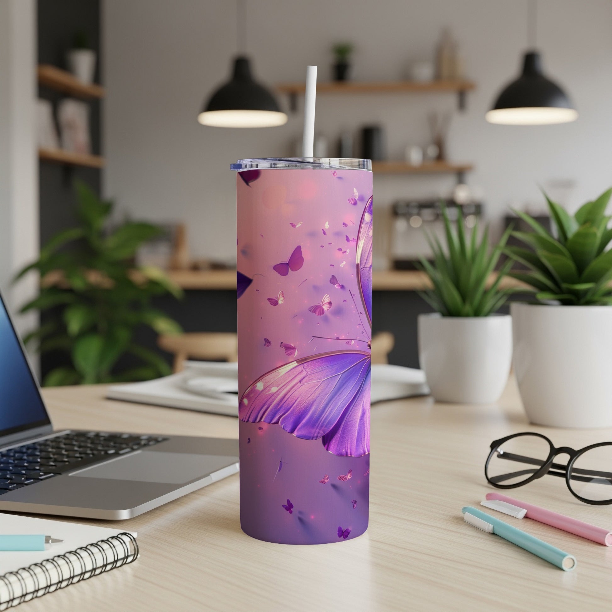 Purple butterfly tumbler with straw on desk with laptop and plants.