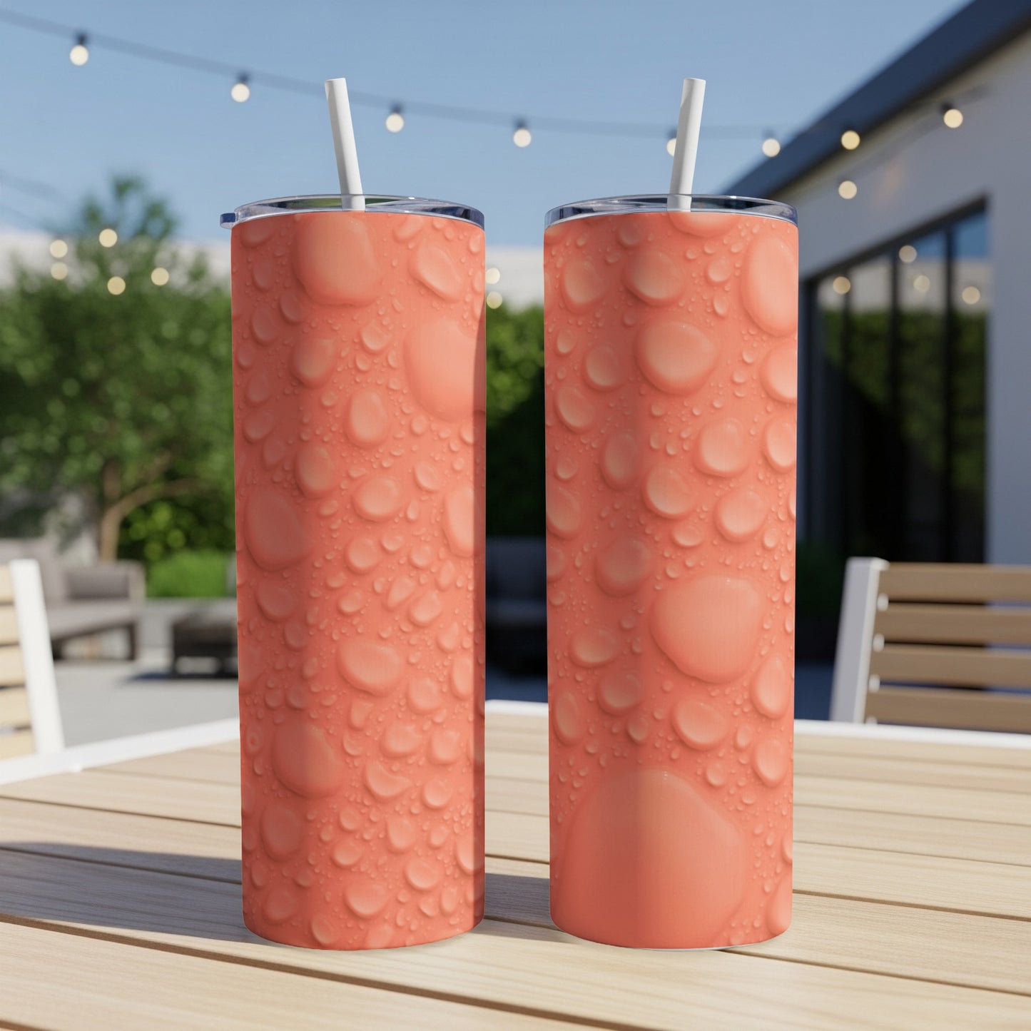 Two coral-colored tumblers with a water droplet pattern on a patio table.