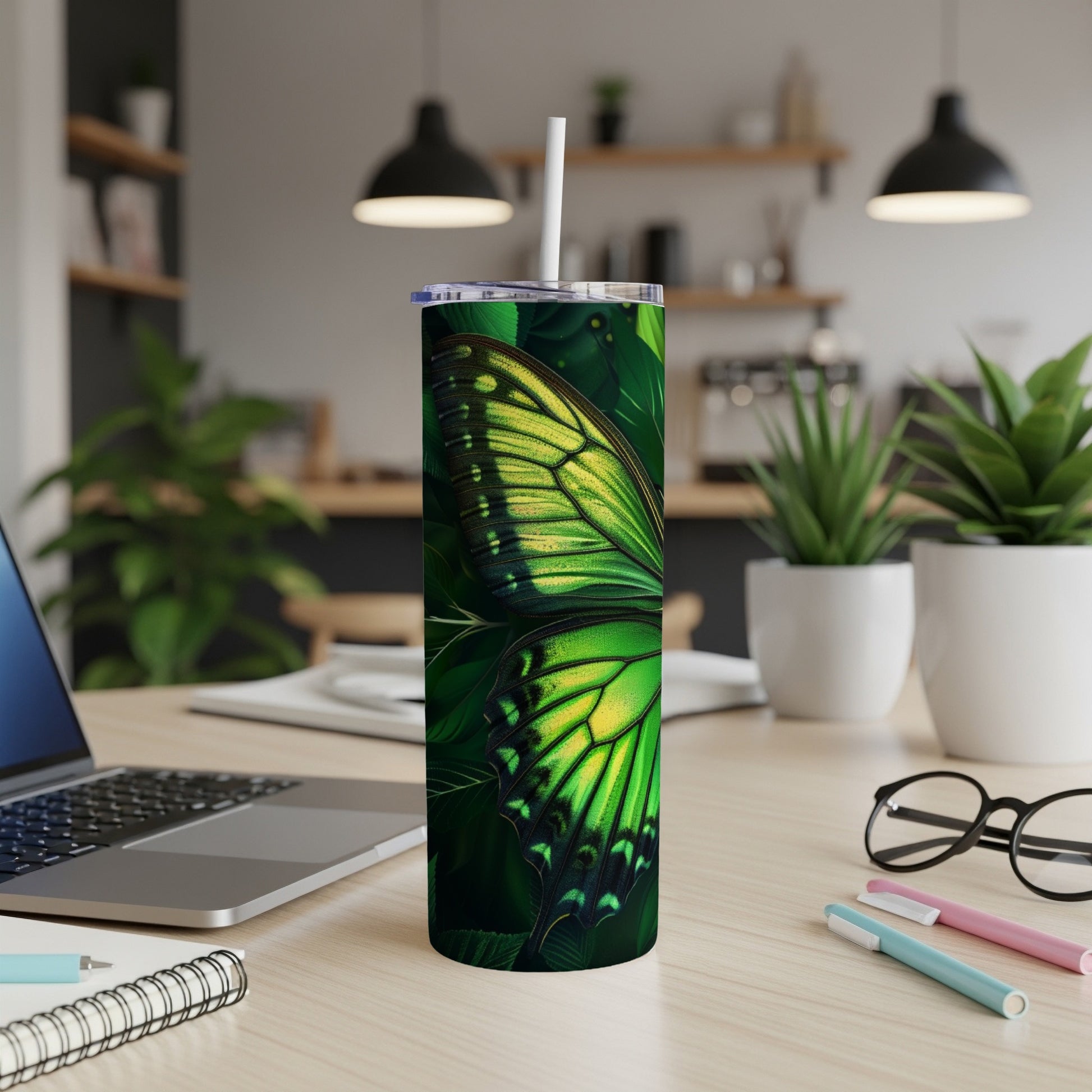 Green butterfly wings on a tumbler with a straw on a desk.