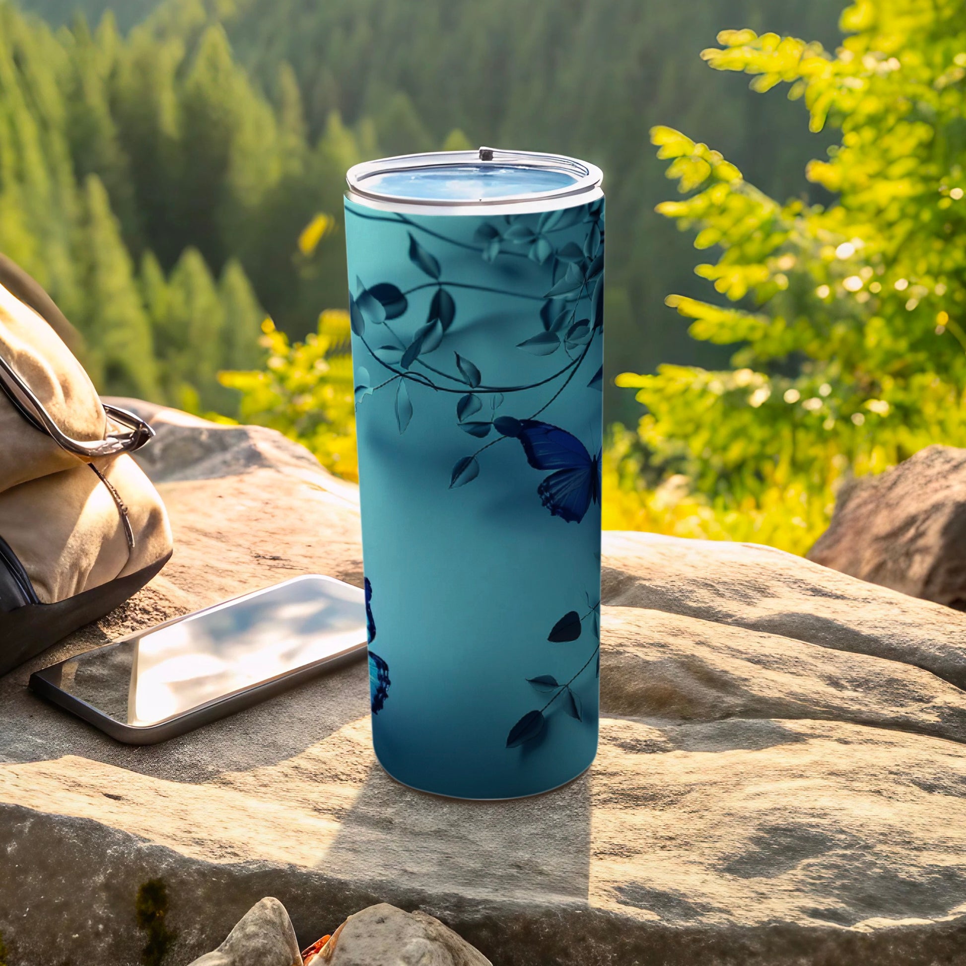 Blue tumbler with floral and butterfly pattern on rocky surface.