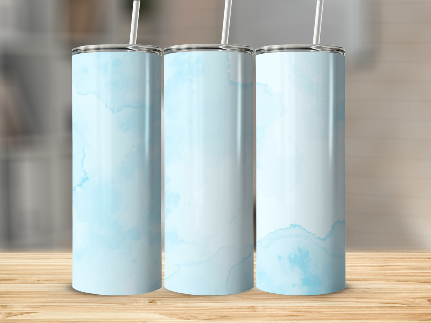 Three light blue marbled tumblers with white straws stand on a wooden surface.