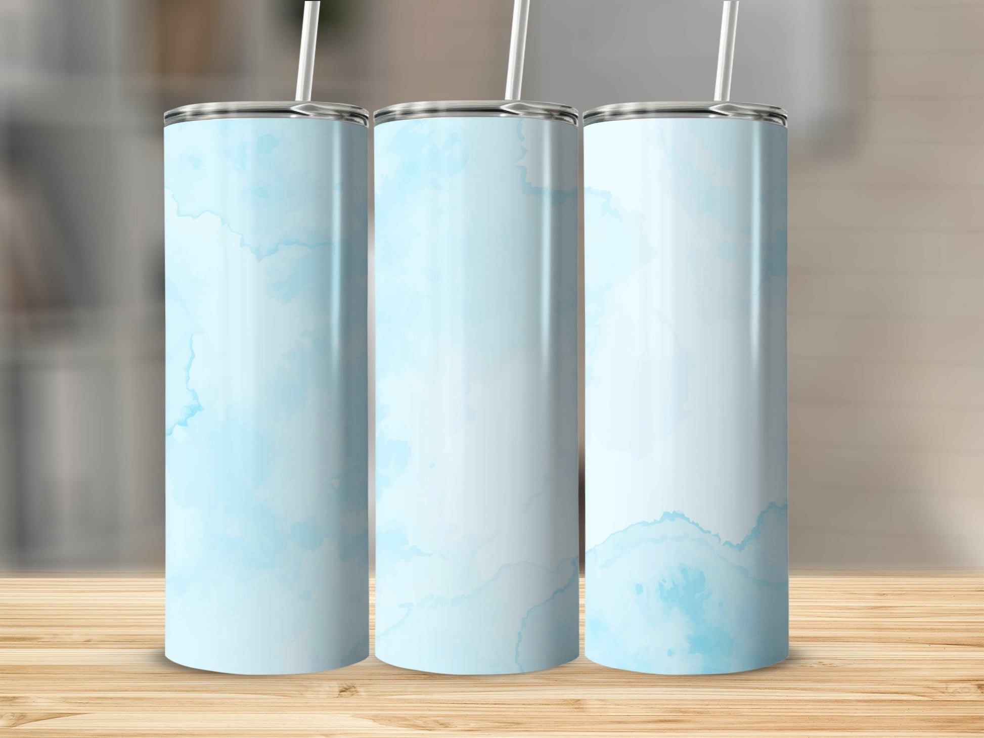 Three light blue marbled tumblers with white straws stand on a wooden surface.