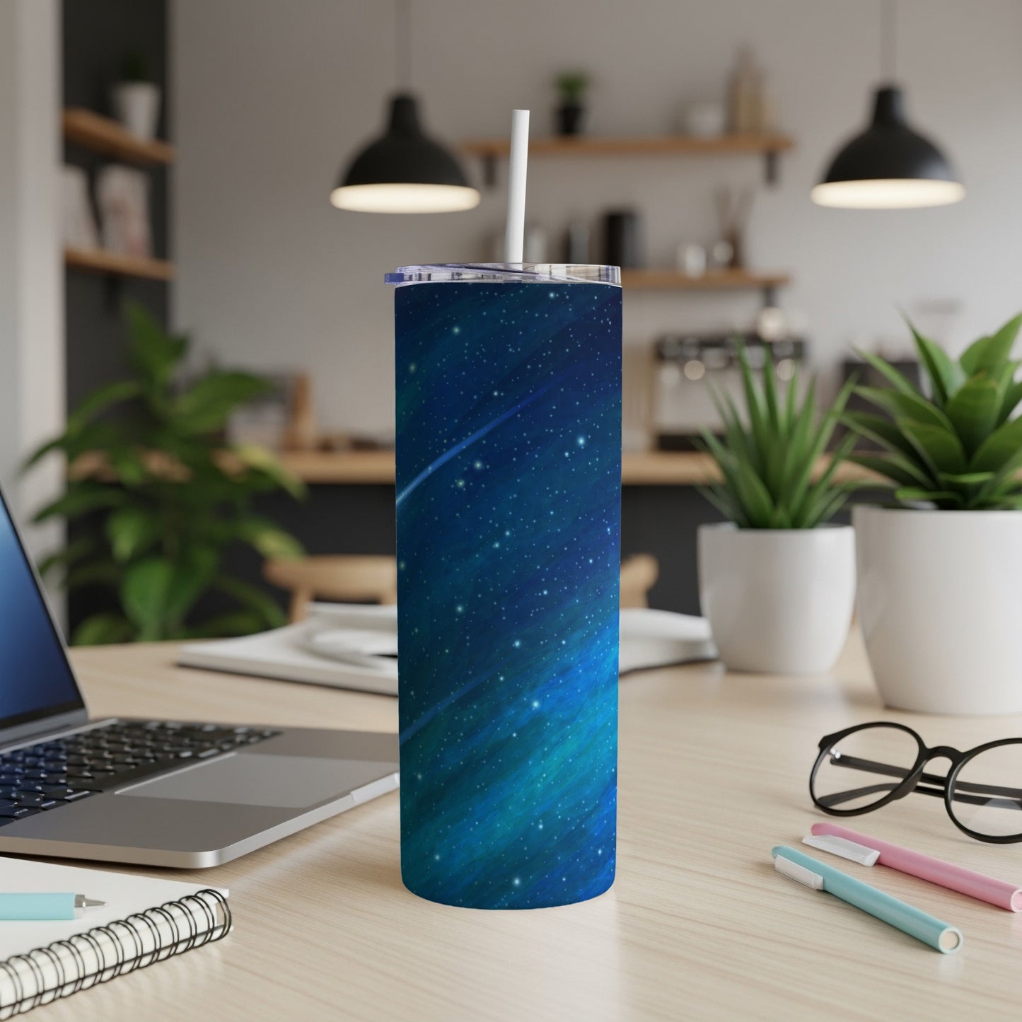 Tumbler with blue and green celestial design and white straw on a wooden desk.