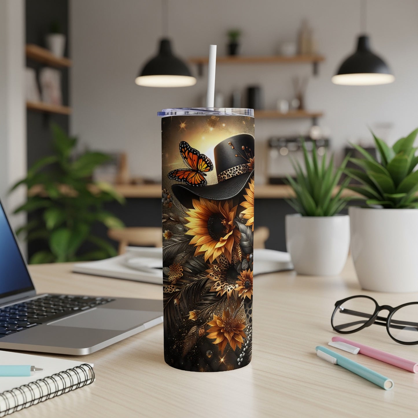 Cowboy hat with sunflowers and butterfly, on a desk with laptop and pens.