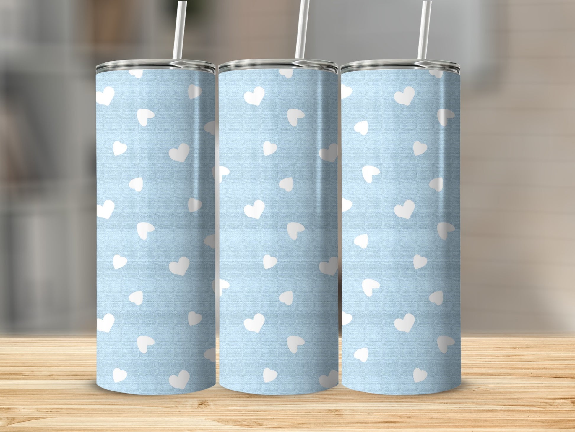 Three tall, light blue tumblers with a repeating white heart pattern and straws.