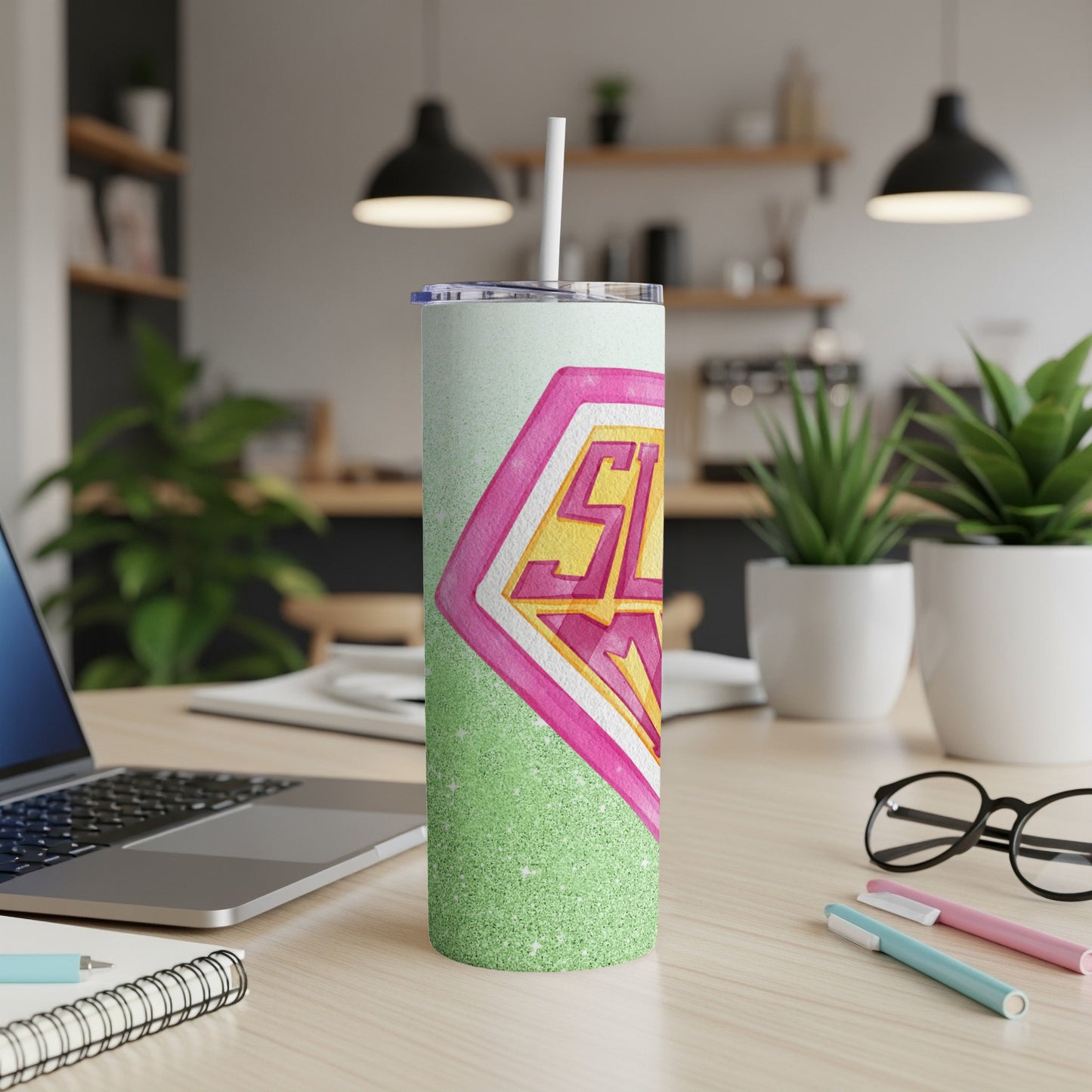 Glittery tumbler with pink and yellow "SL" logo on a desk.