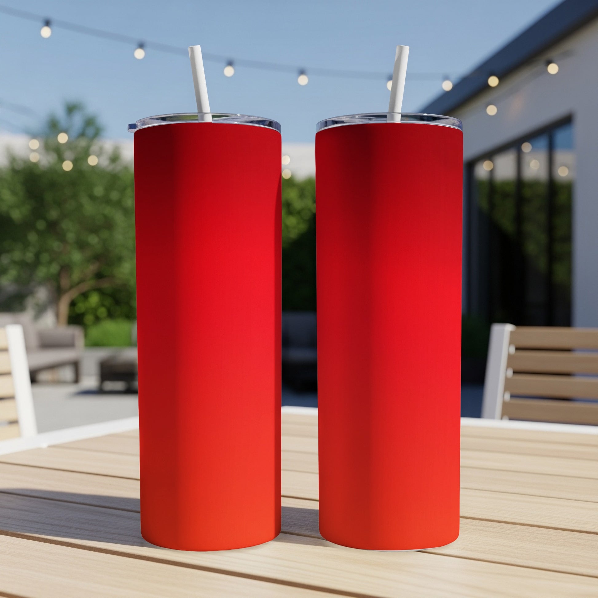 Two tall, red gradient stainless steel tumblers with straws on a wooden table.