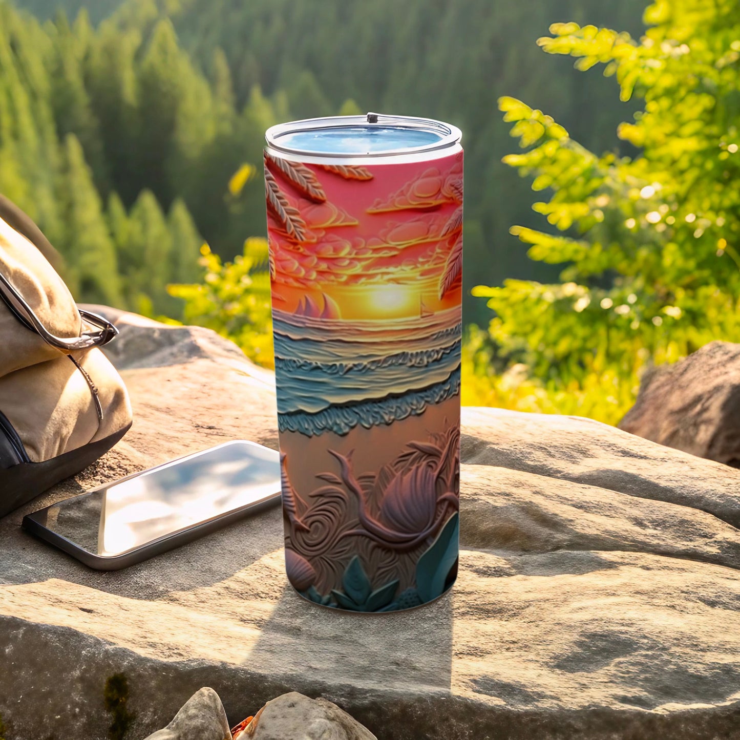 Tumbler with a sunset beach scene design, resting on rocks near a backpack and phone.