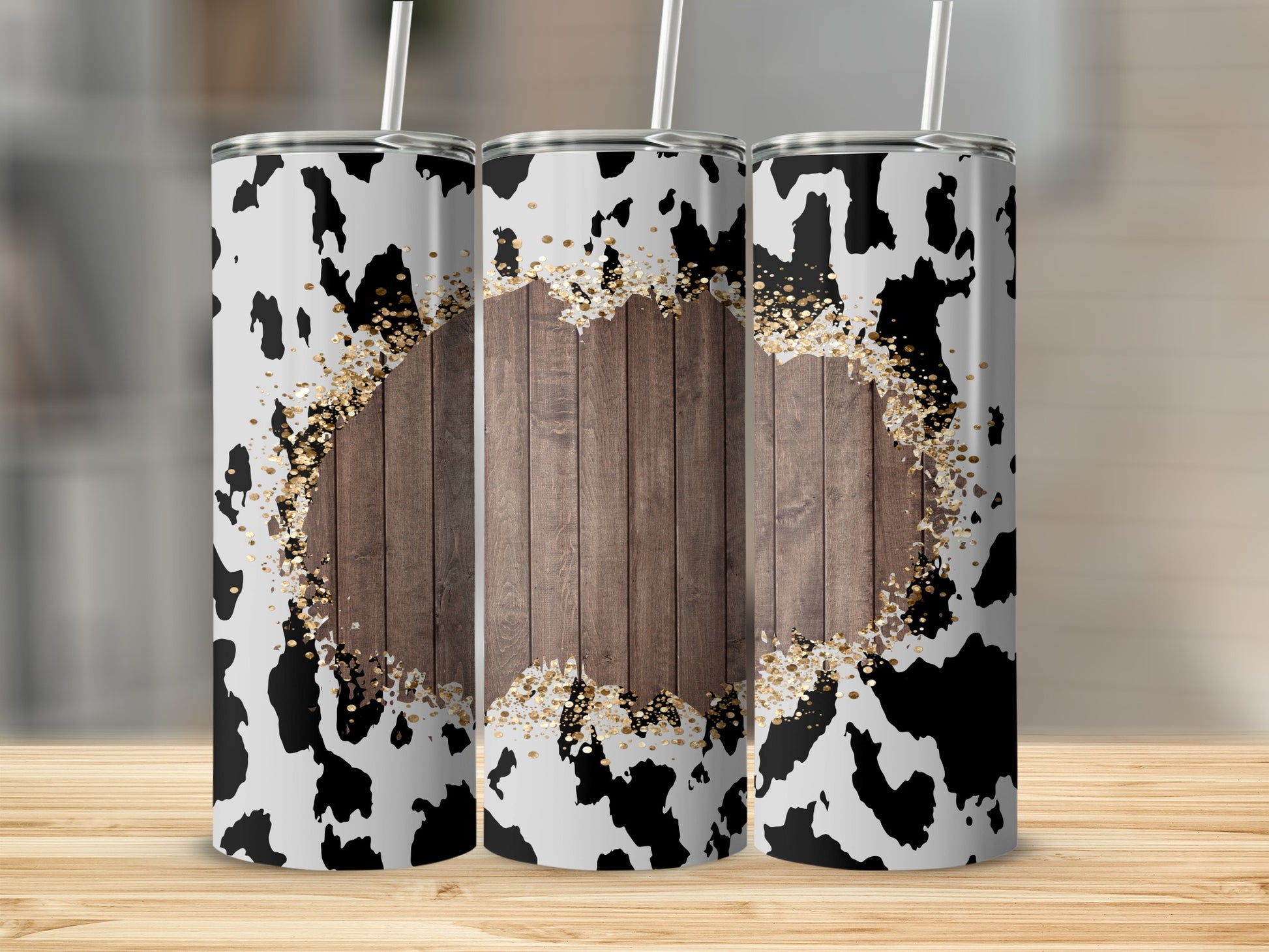 Three tumblers with cow print and gold glitter design on a wooden surface.