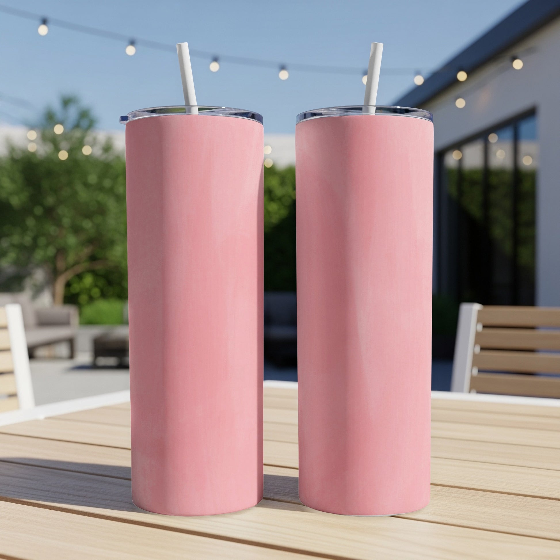 Two pink stainless steel tumblers with straws on a wooden table.