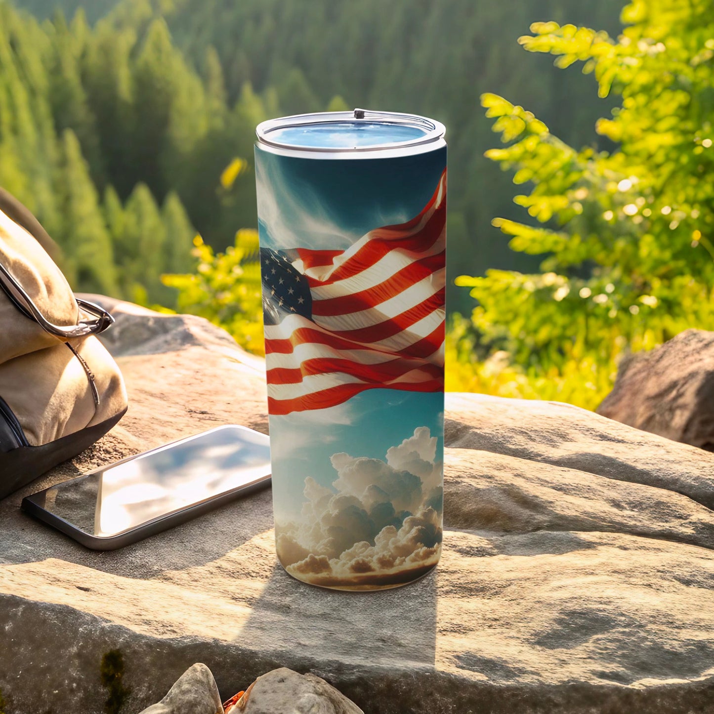 American flag tumbler with clouds on rocks with phone and bag.