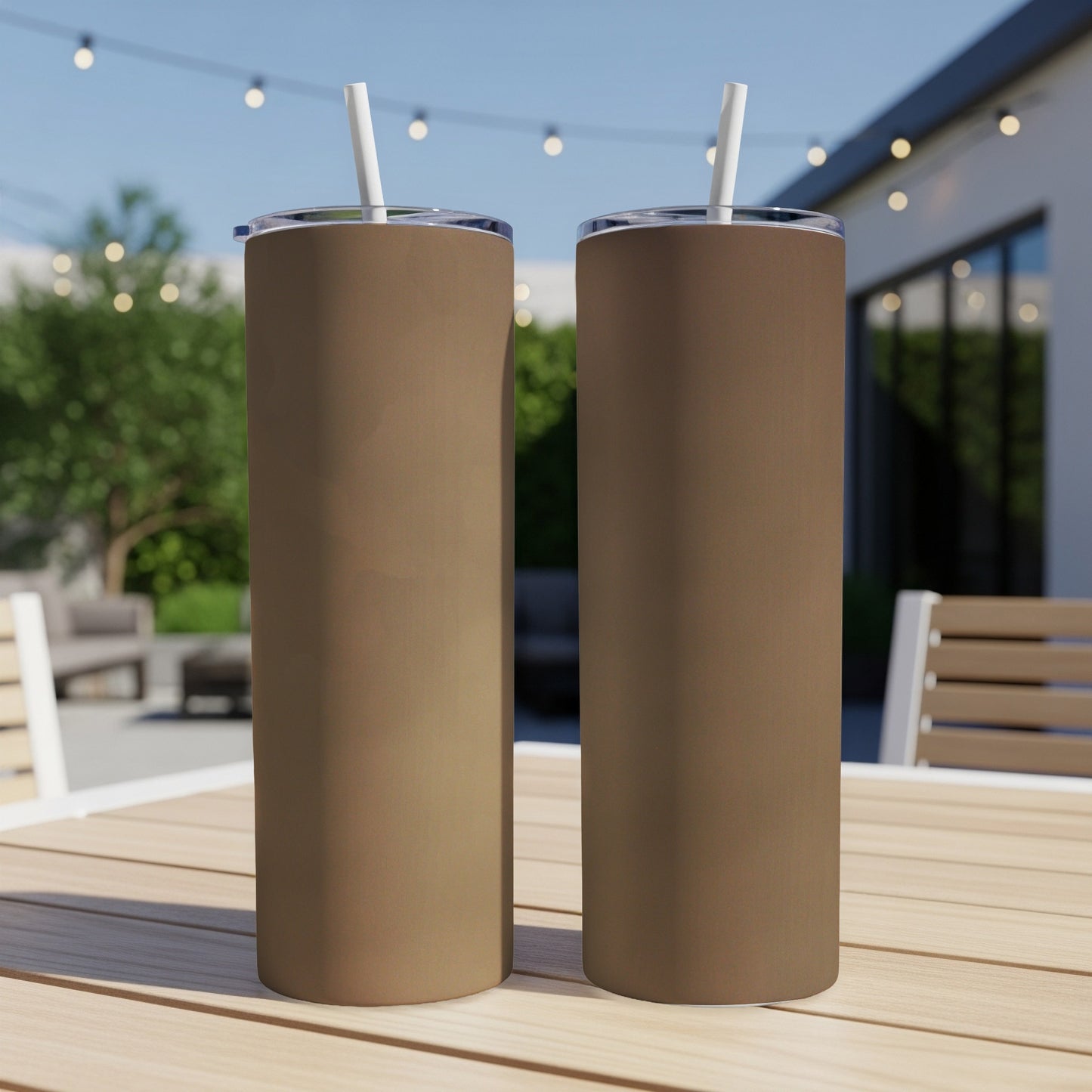Two brown tumblers with white straws on a wooden table outdoors.