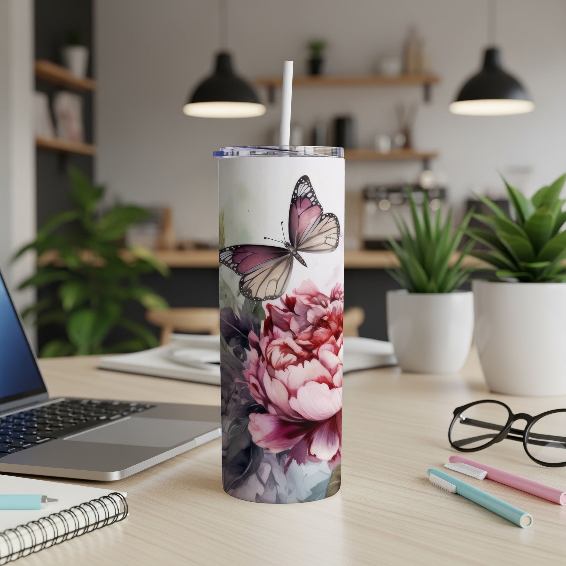 White tumbler with butterfly and floral design, on desk with laptop and pens.
