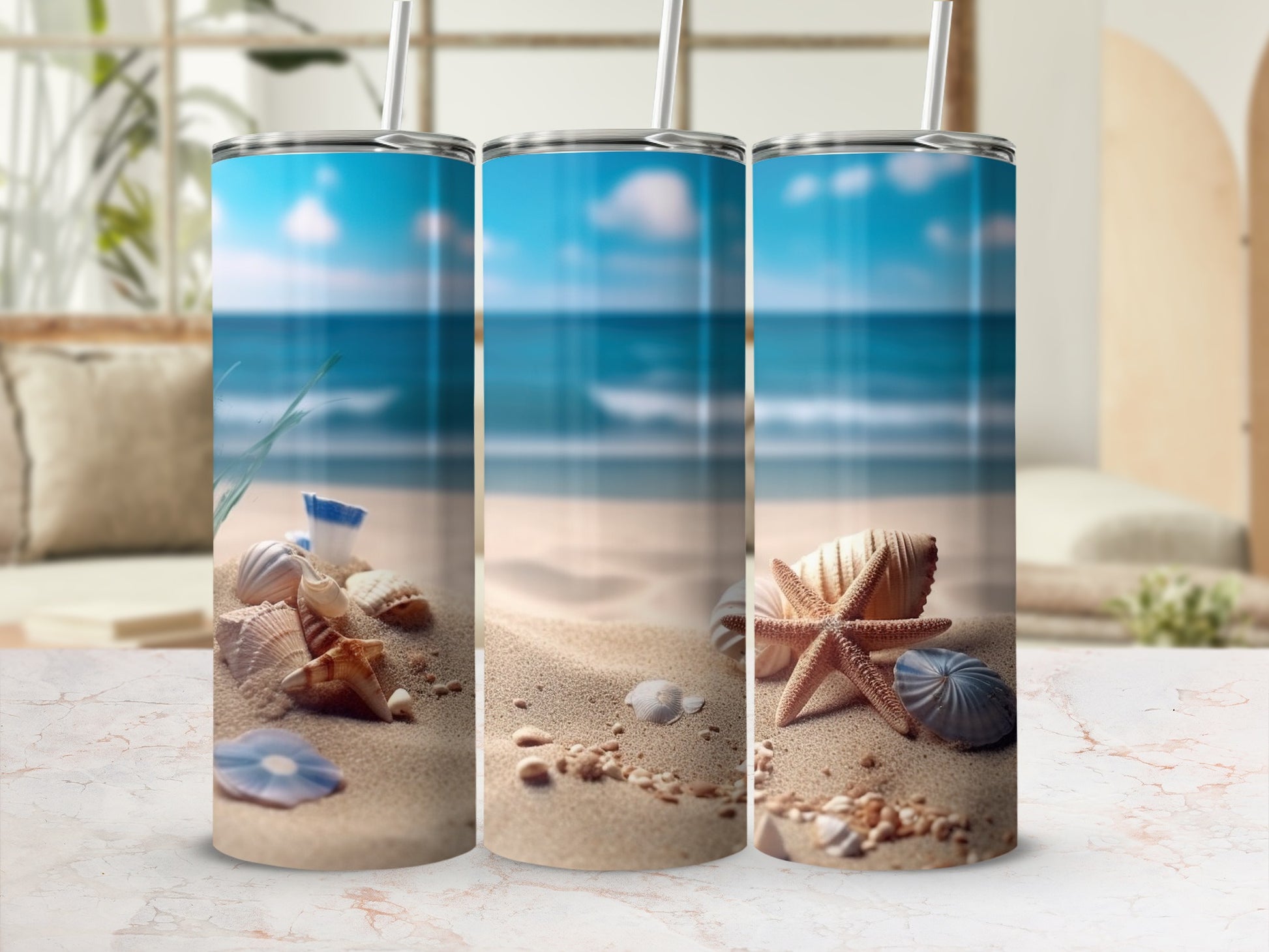 Three tumblers with beach and seashell designs on a sandy beach.