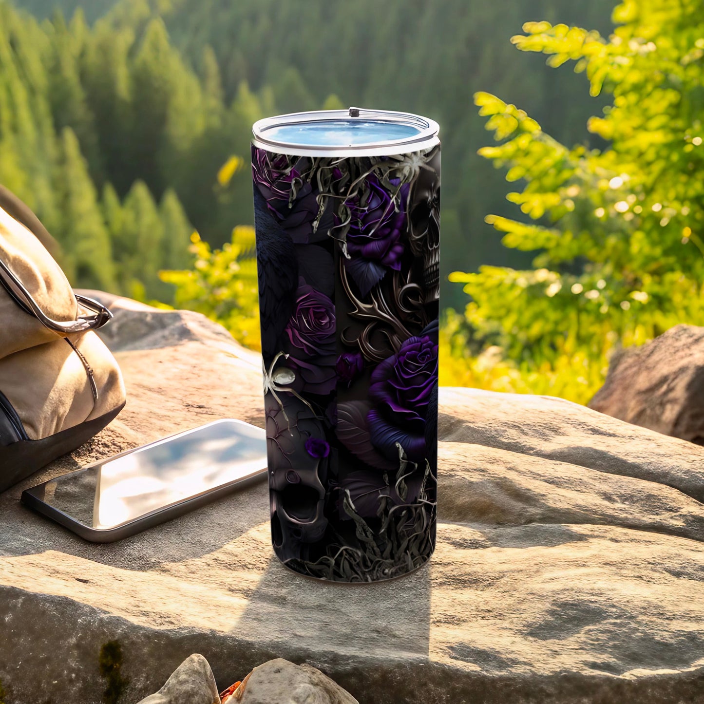 Black tumbler with purple roses, skulls, and cobwebs, resting on rocks.
