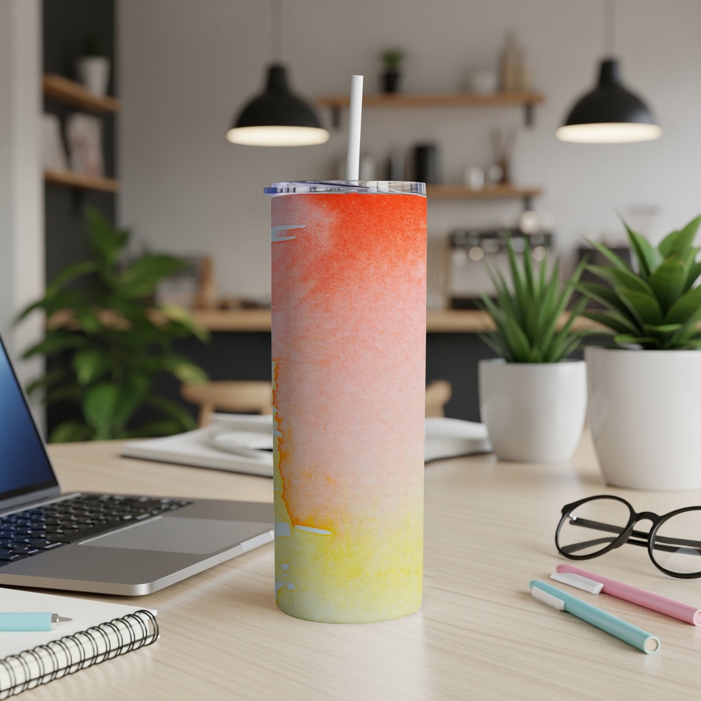 Tall tumbler with a watercolor sunset design sits on a desk.
