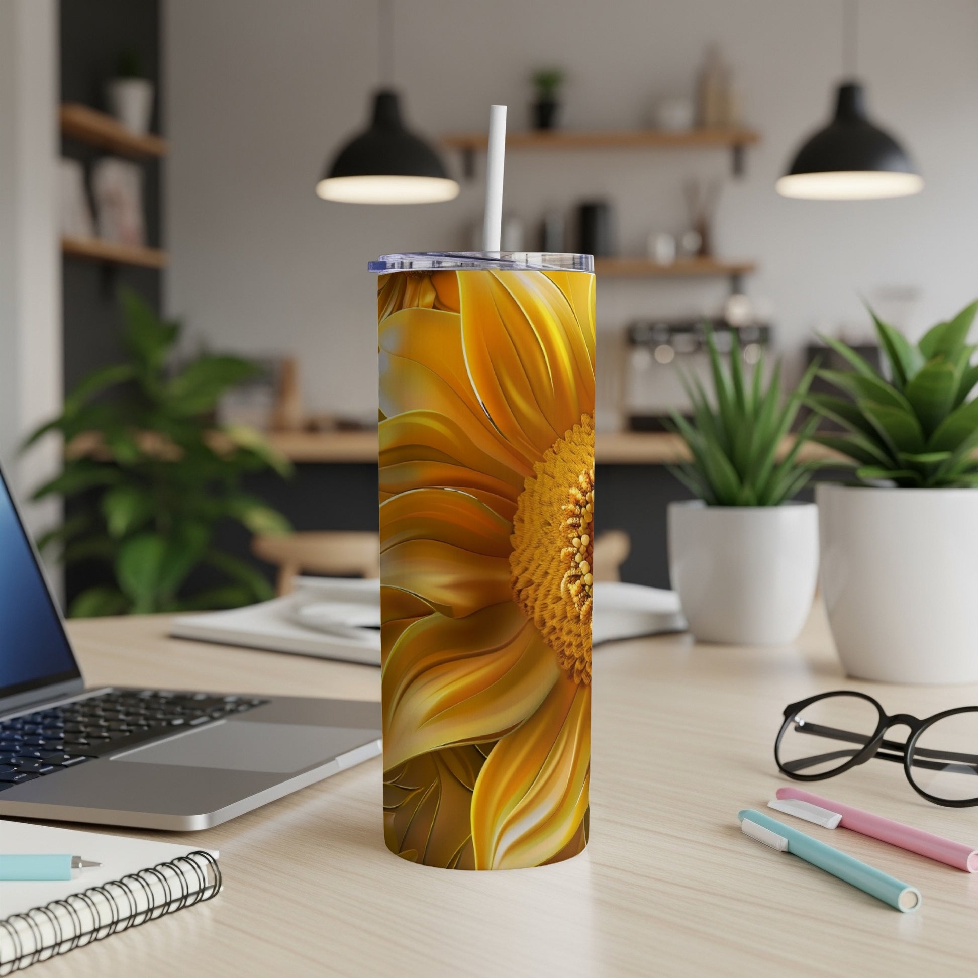 Sunflower tumbler with straw on a desk, with laptop and pens.