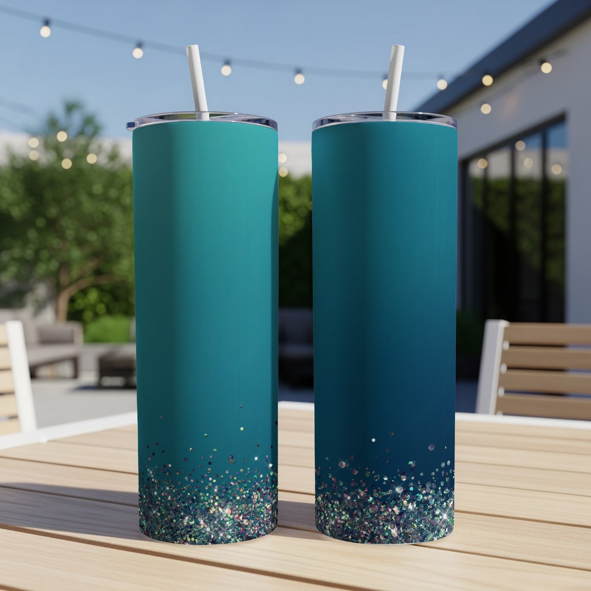 Two teal tumblers with glitter at the base and white straws are on a table.