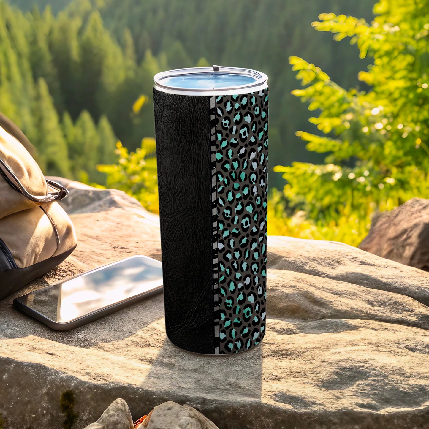 Black and teal leopard print tumbler on rock with phone and backpack.