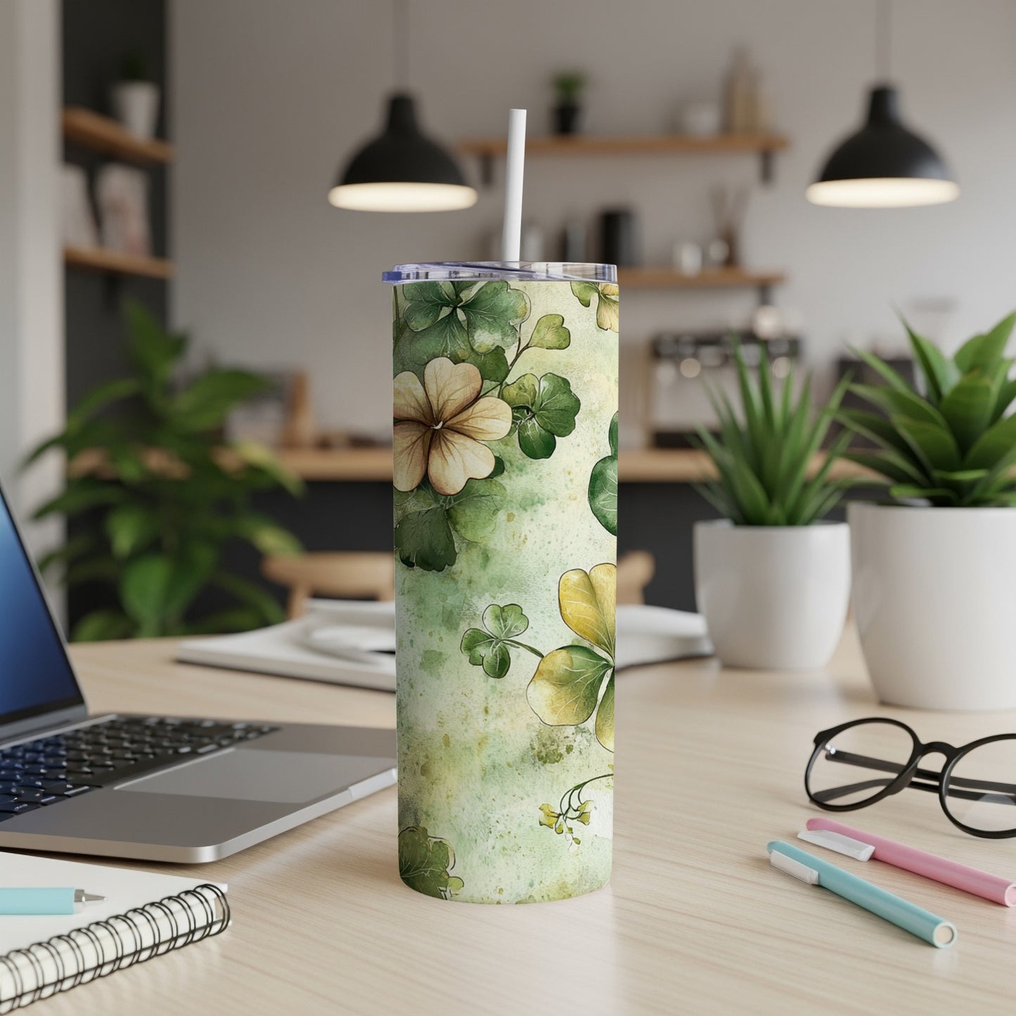 Green watercolor shamrock and floral tumbler with straw on desk.