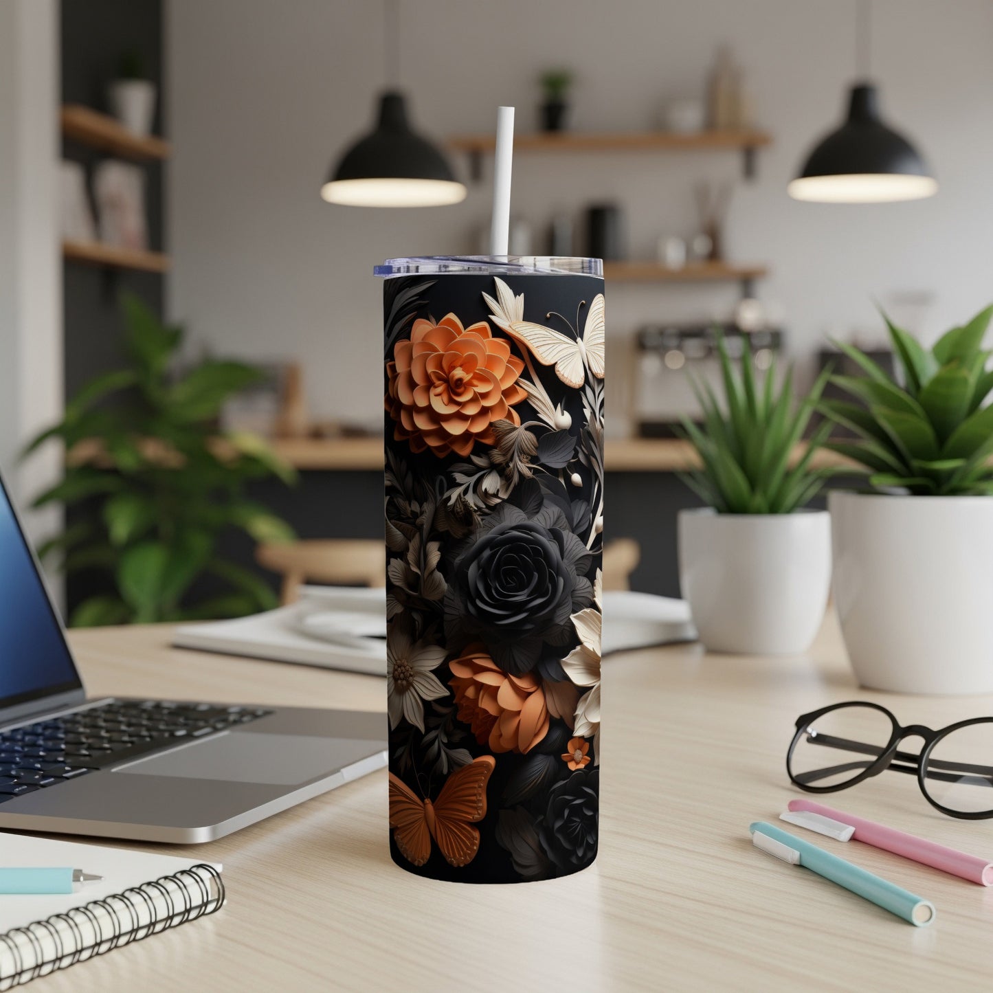 Black tumbler with floral and butterfly design on a desk with a laptop.