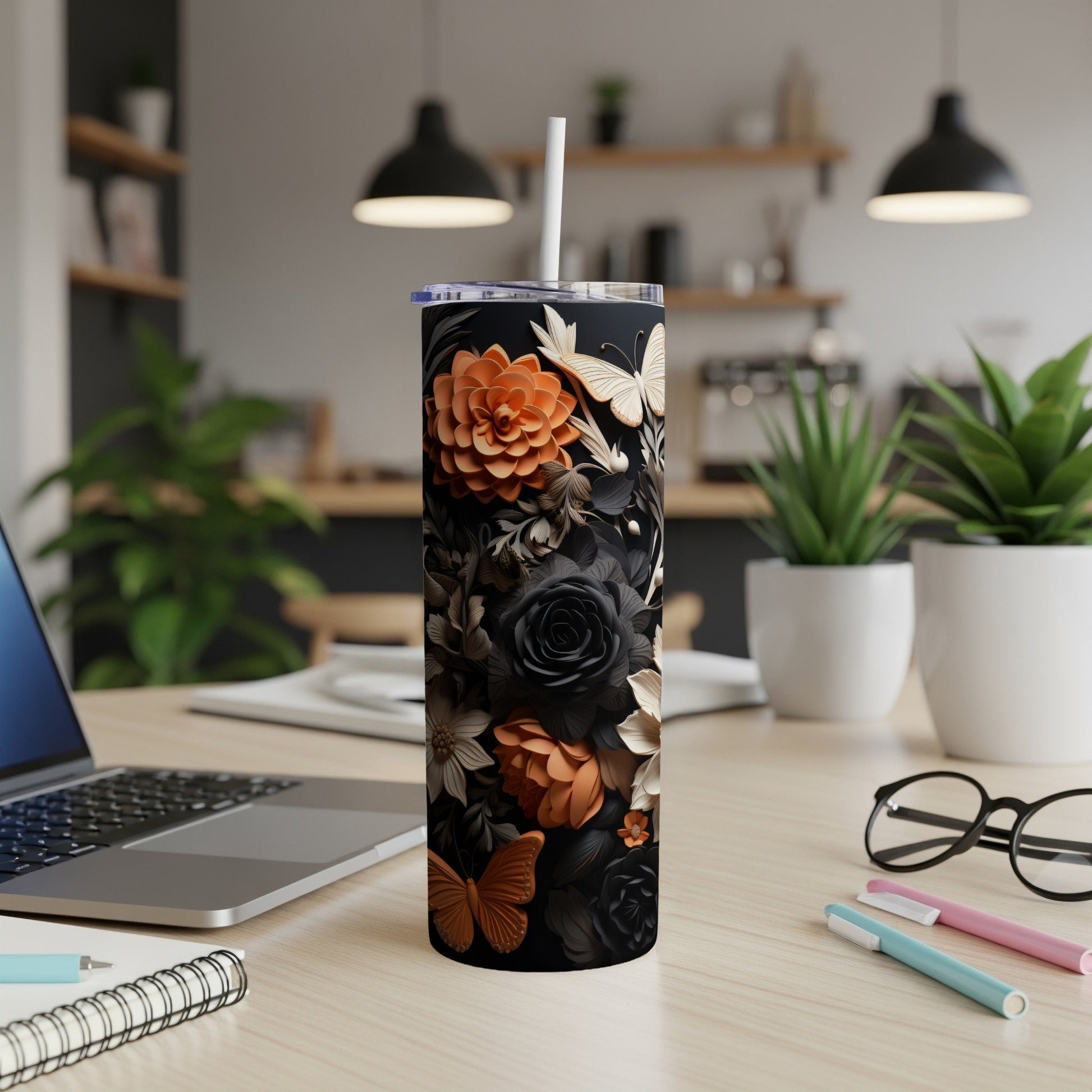 Black tumbler with floral and butterfly design on a desk with a laptop.