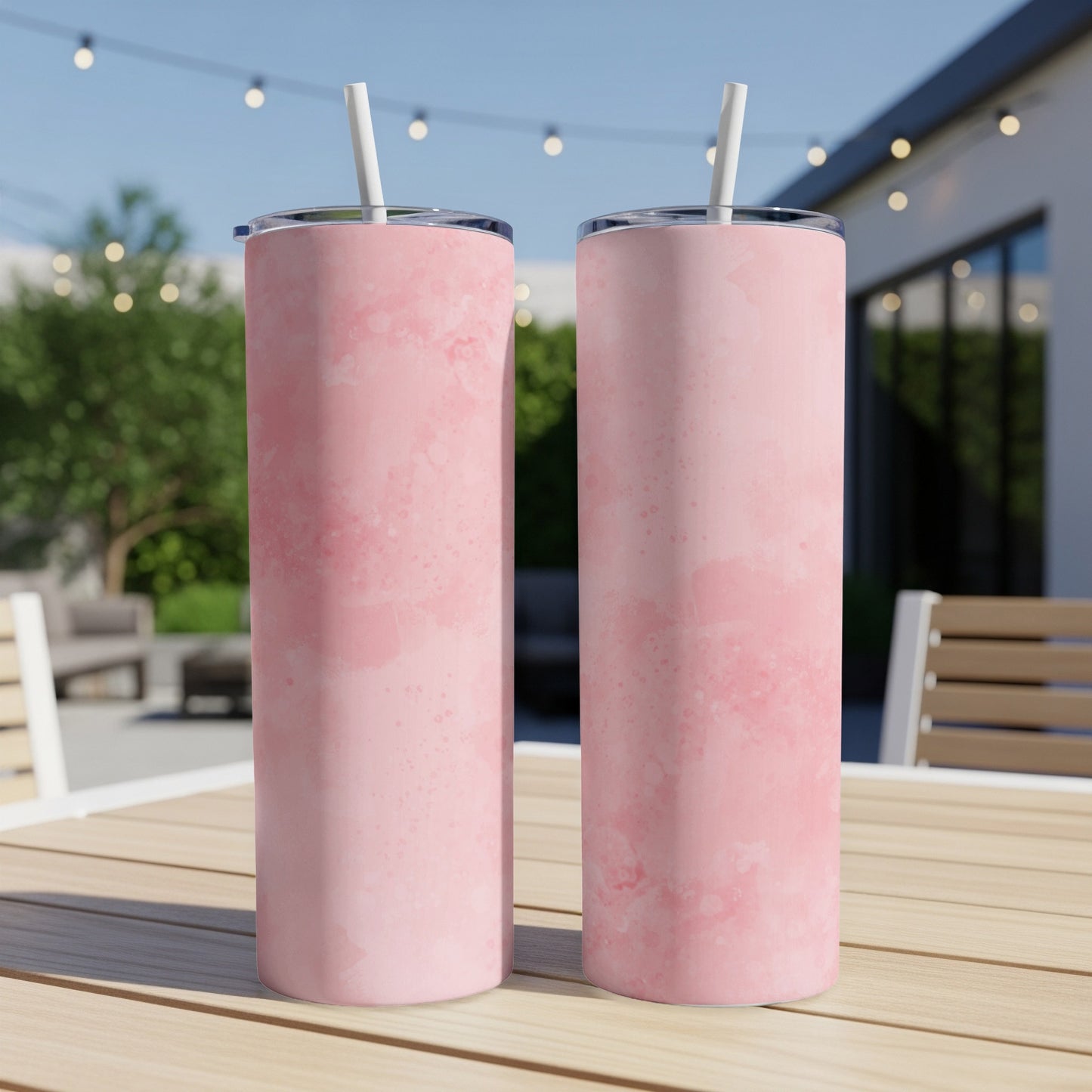 Two pink marble pattern tumblers with straws on a wooden table outdoors.