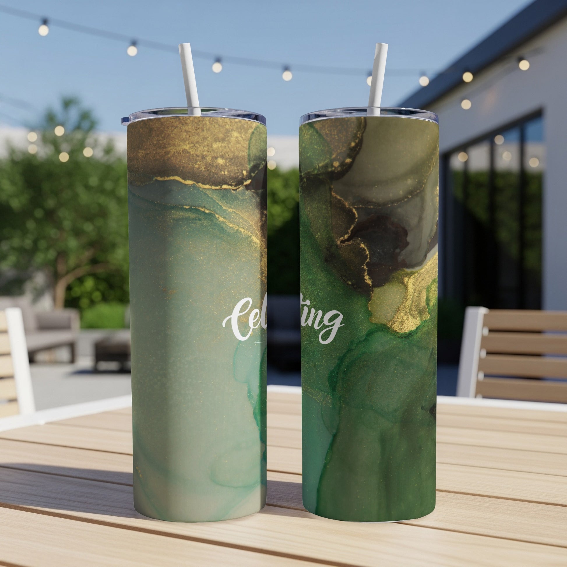 Two green and gold tumblers with "Celebrating" text on outdoor table.