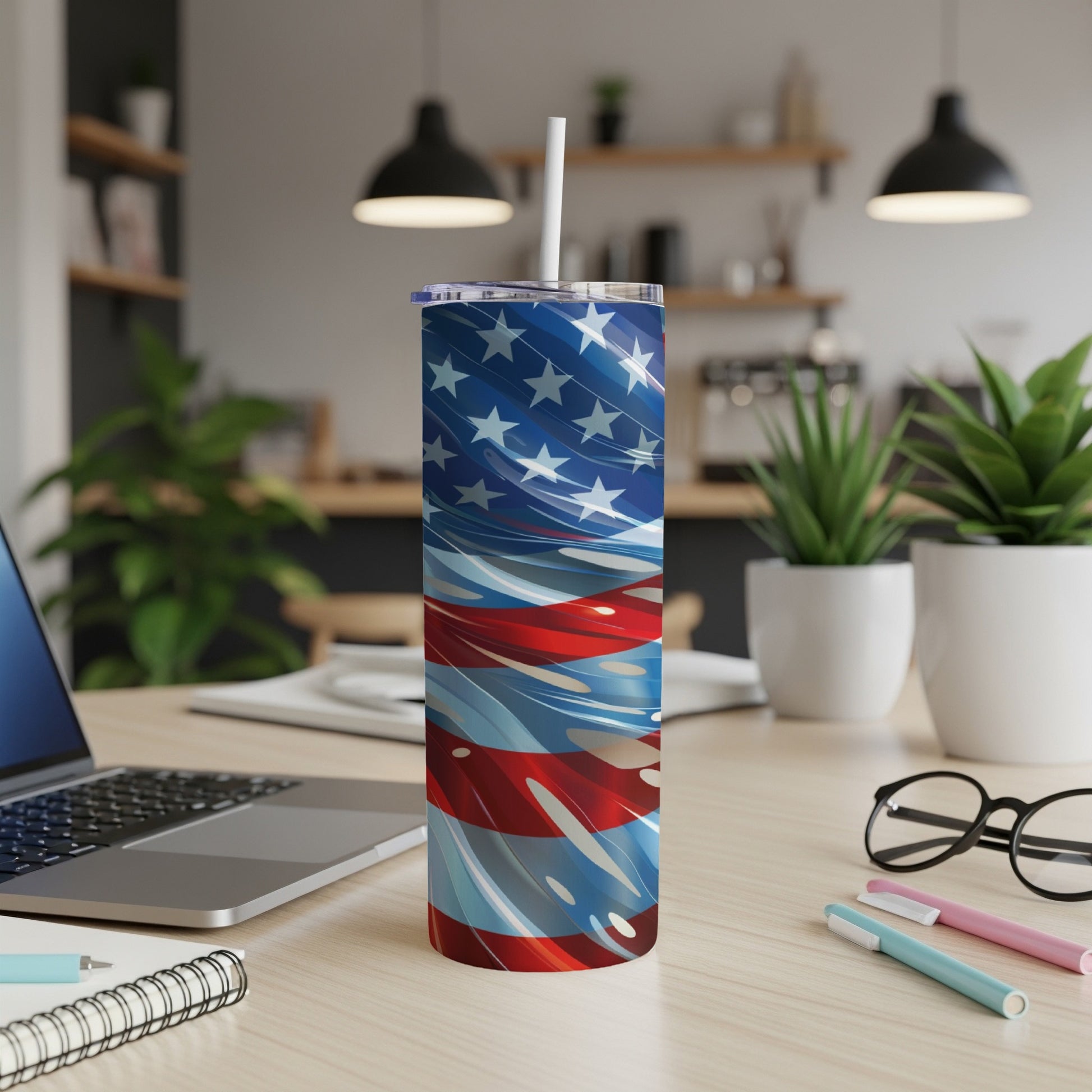Tall tumbler with American flag design and straw on a wooden desk.