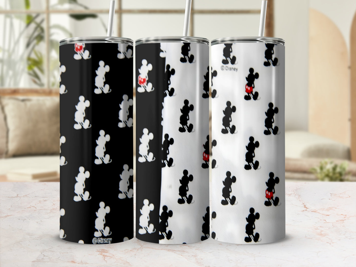 Three Disney Mickey Mouse tumblers with straws on a textured surface.