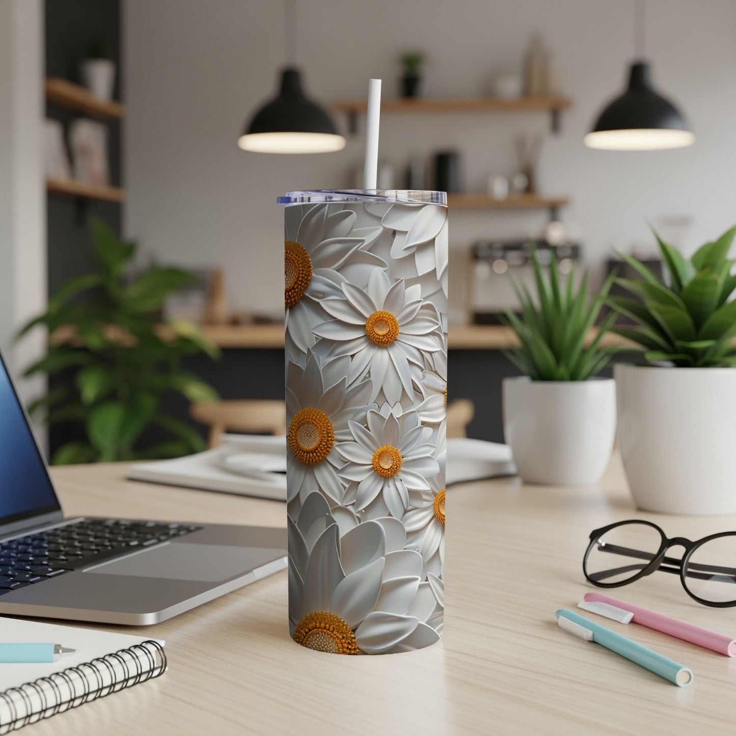 White and gold floral pattern on a tall tumbler with a straw, on a desk.